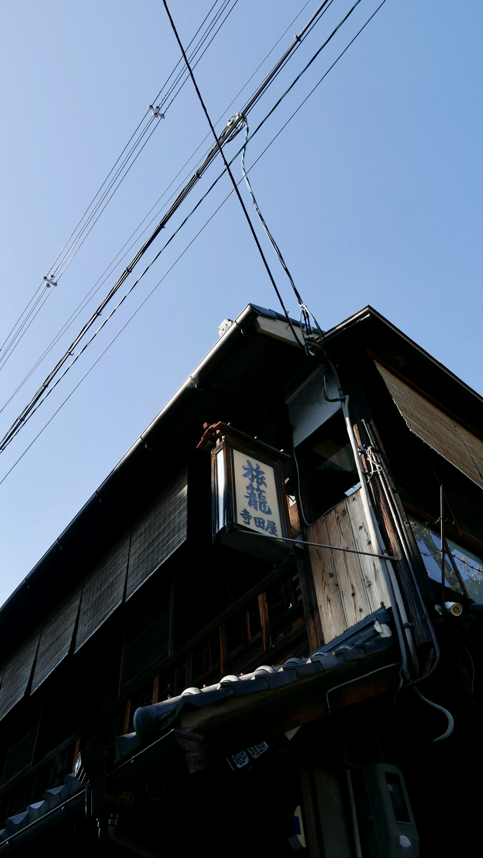 Coin d'un bâtiment japonais traditionnel sous un ciel bleu avec des lignes électriques