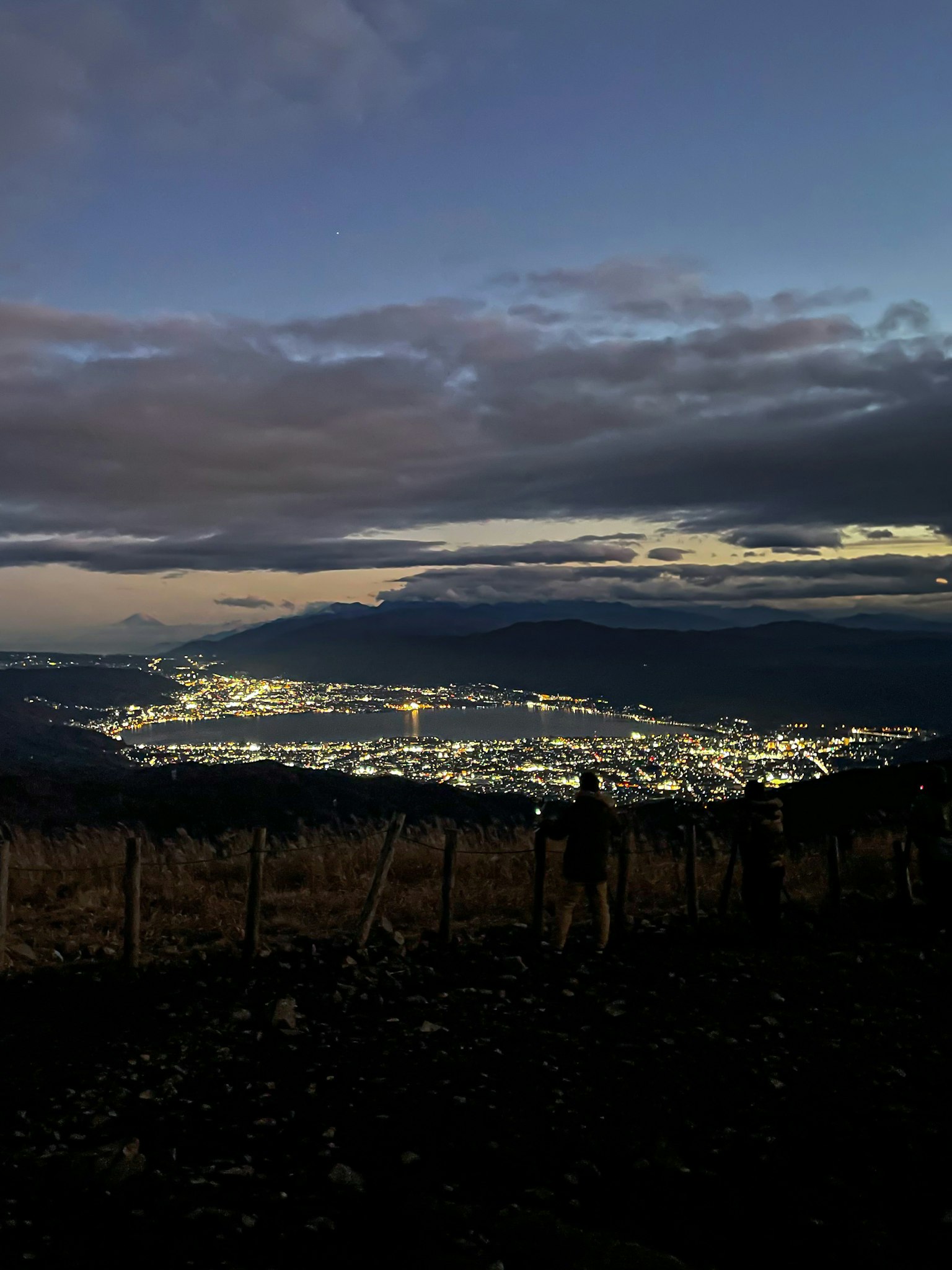 Luci della città di notte con nuvole e montagne in lontananza