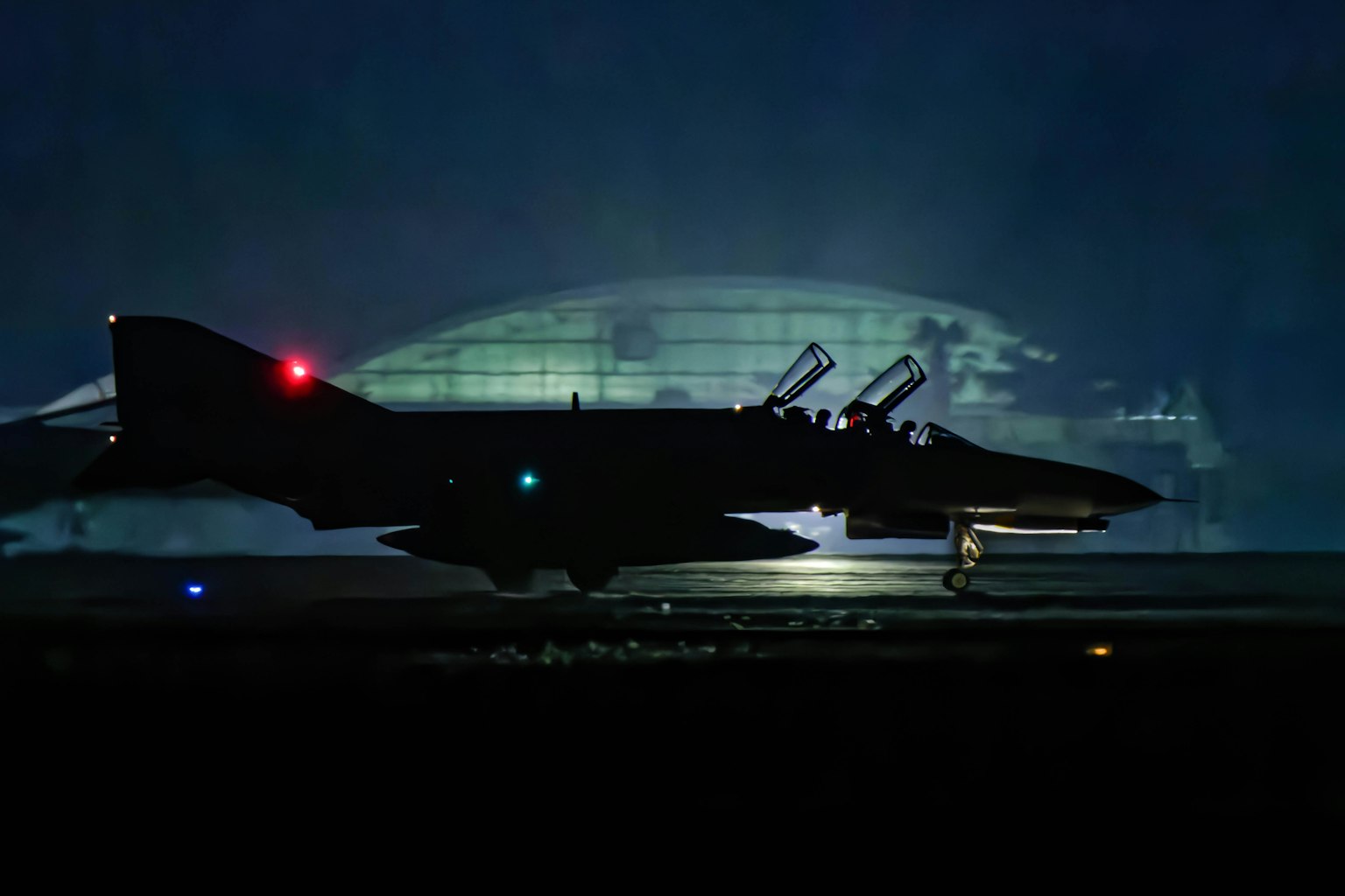 Silhouette eines F-4-Jets bei Nacht mit einem Hangar im Hintergrund