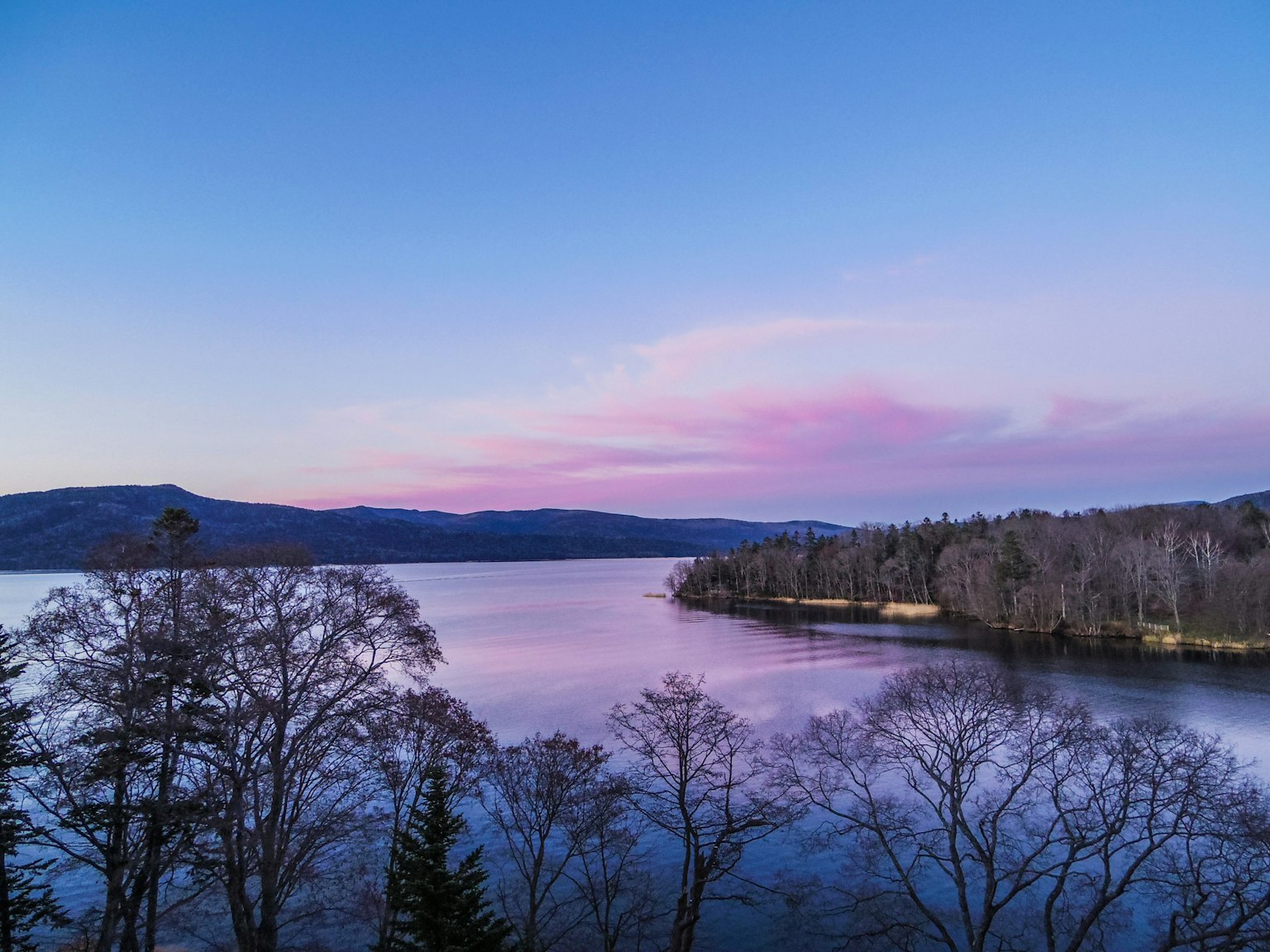 Malersiche Aussicht auf einen blauen See mit rosa Wolken und Bäumen am Ufer