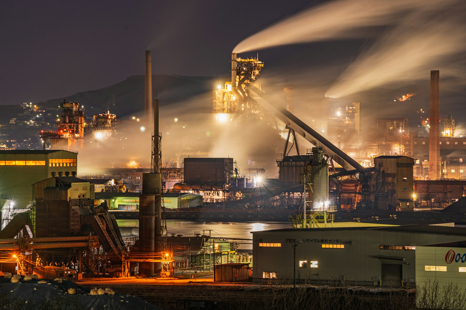 Nächtliche Industrieszene mit Fabriken, die Rauch und Dampf abgeben, sichtbar Maschinen