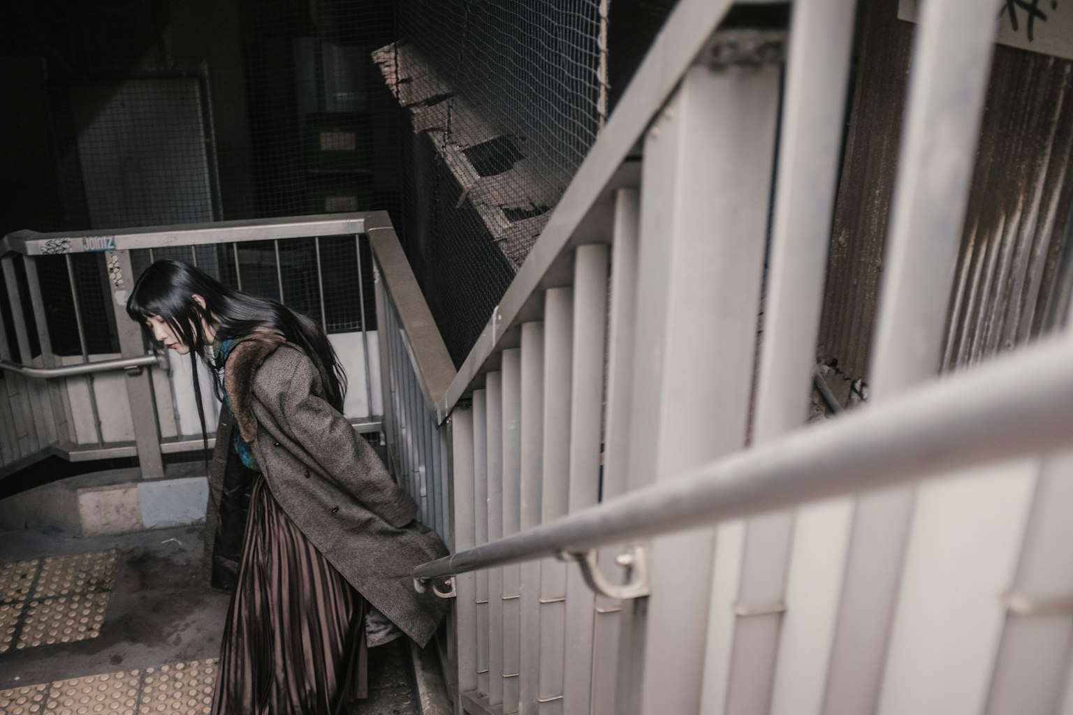 Une femme descendant un escalier sombre portant un long manteau