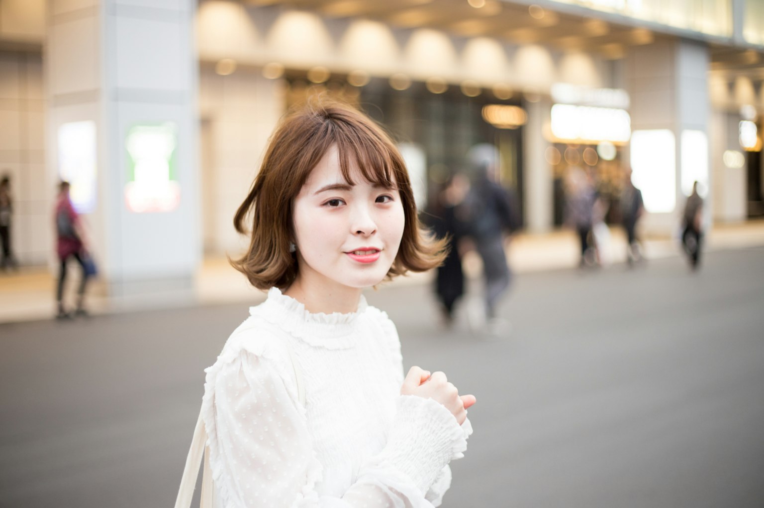 A woman in a white blouse smiling in a city street scene