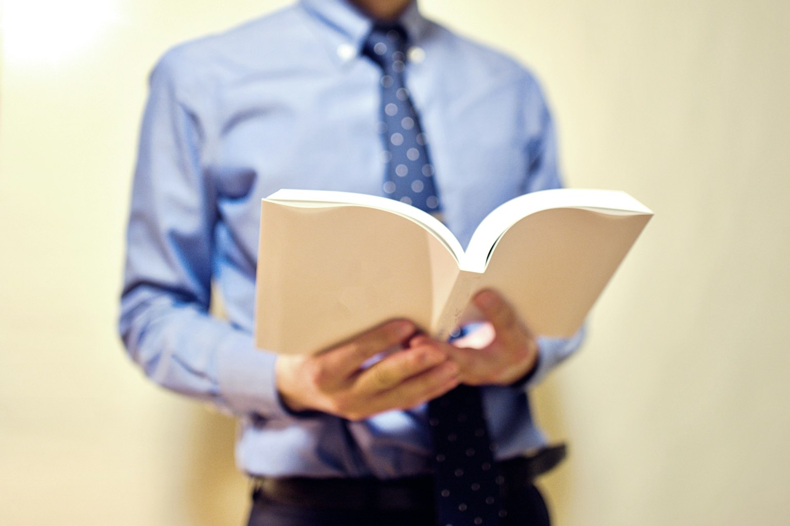 Hombre con camisa azul y corbata sosteniendo un libro abierto