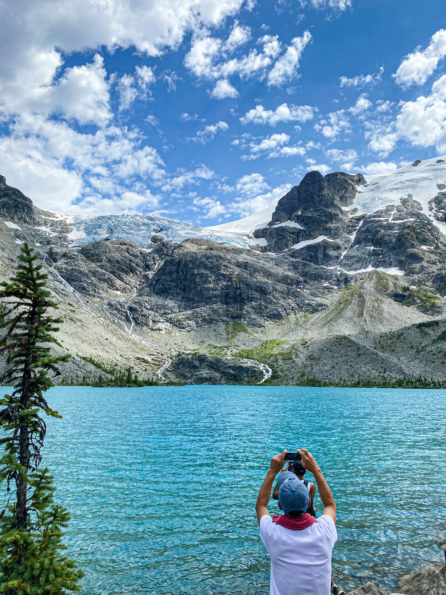 A person taking a photo with a stunning mountain and blue lake backdrop