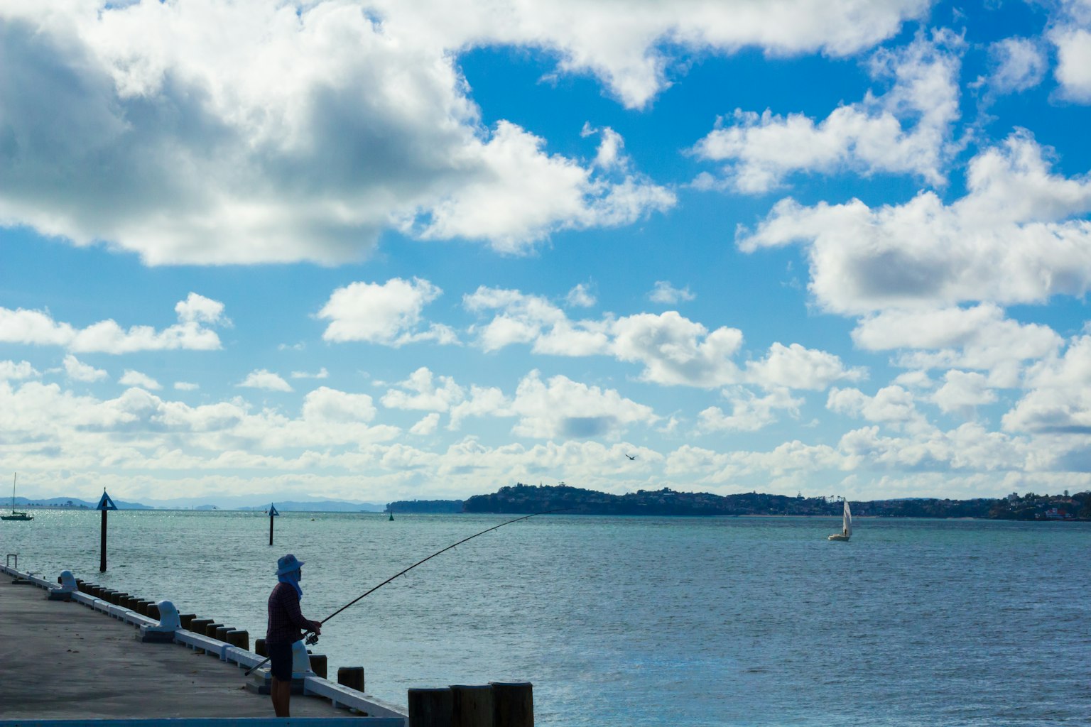 Personne pêchant au bord de l'eau sous un ciel bleu avec des nuages