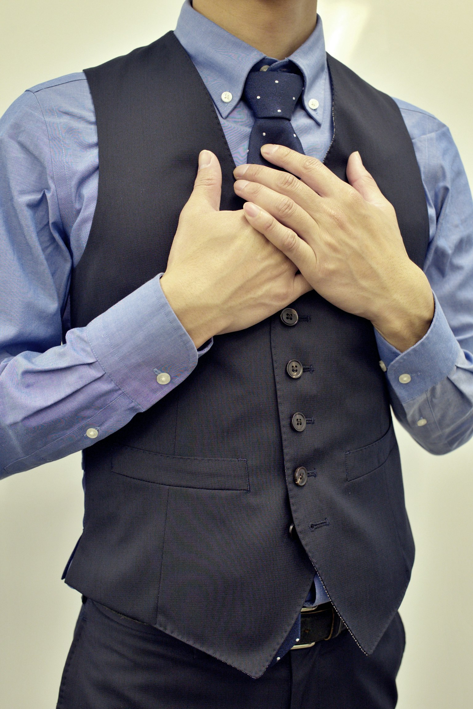 A man wearing a suit vest with his hands placed on his chest
