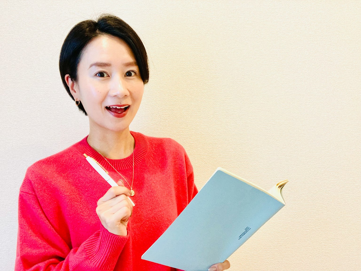 女性微笑着手持蓝色笔记本和钢笔