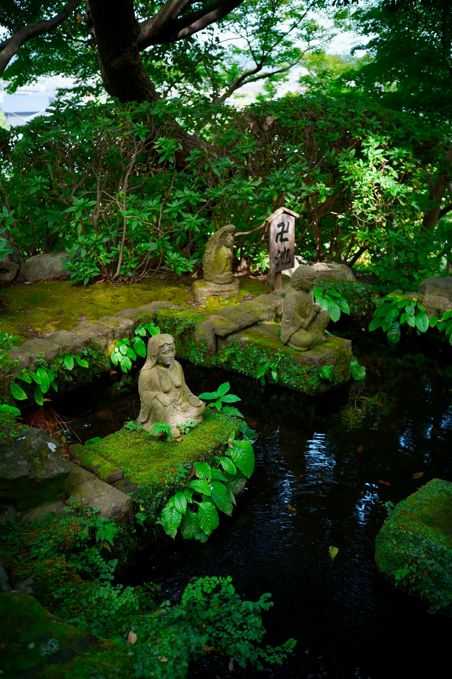 Scenic view of stone statues and pond in a lush garden