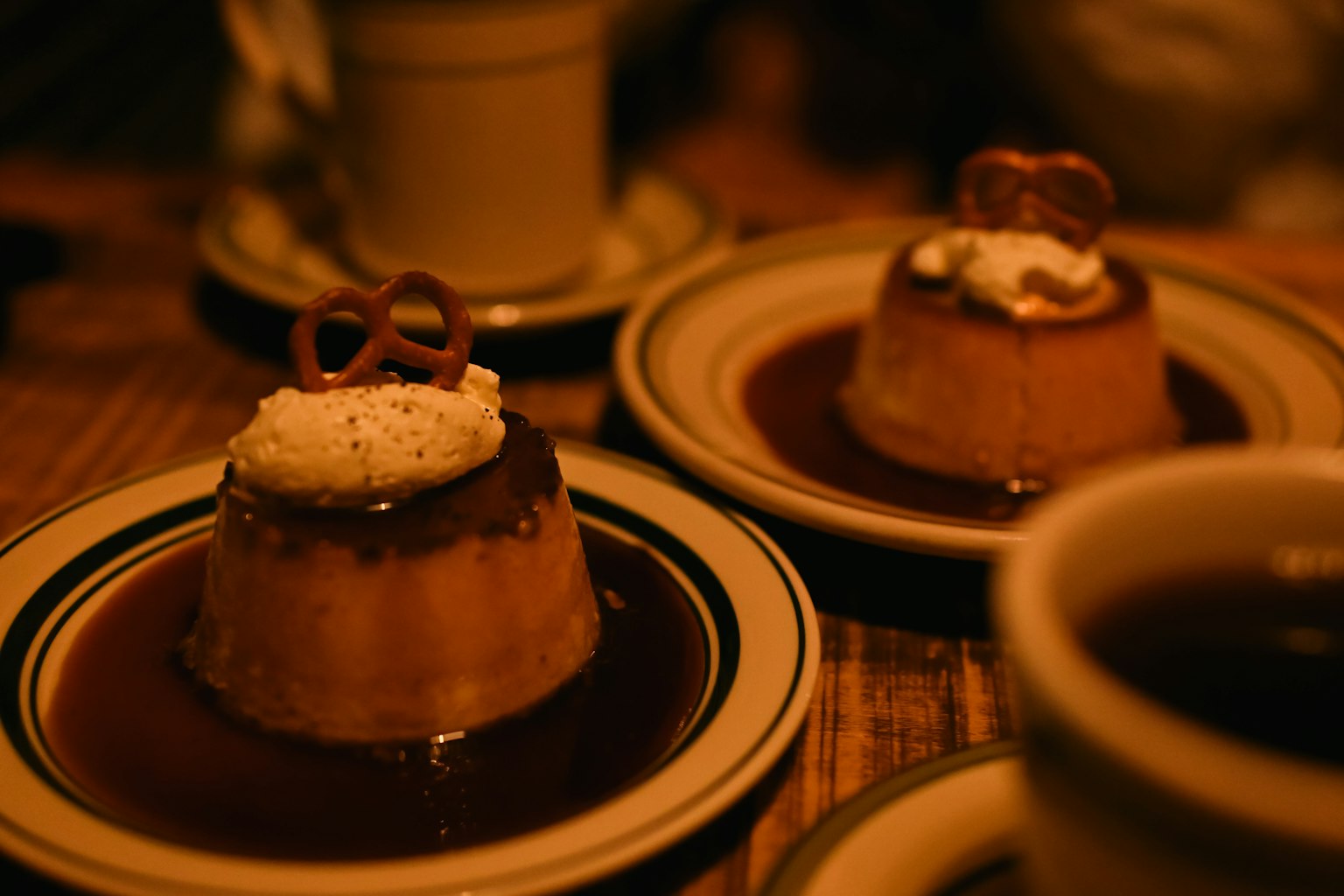 Due porzioni di flan con panna montata e pretzel in un piatto con caffè sullo sfondo