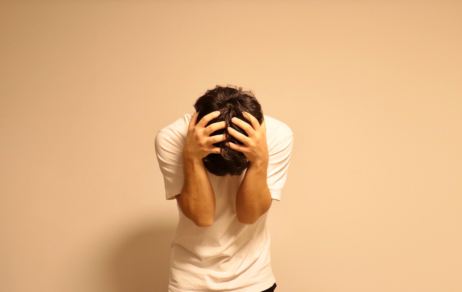 A man holding his head in distress against a plain light-colored background