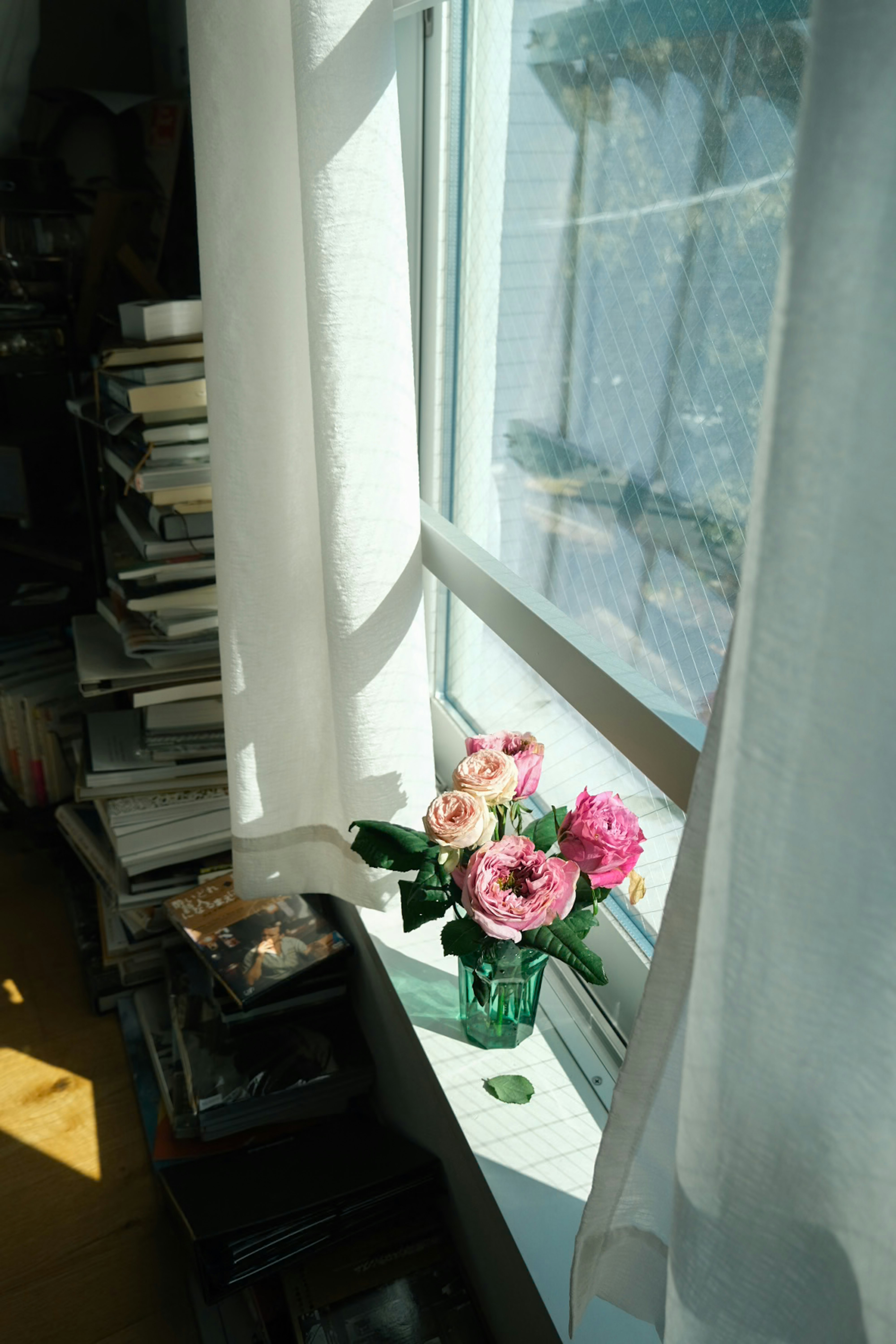 窓辺の花瓶に生けられた薔薇と積読のある部屋