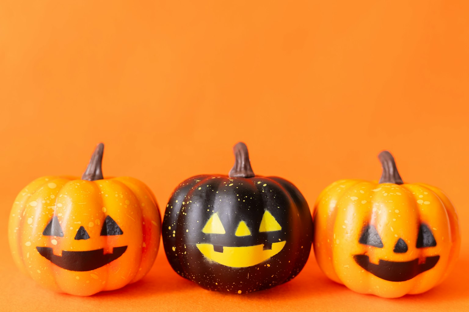 Tiga labu jack-o'-lantern Halloween di latar belakang oranye