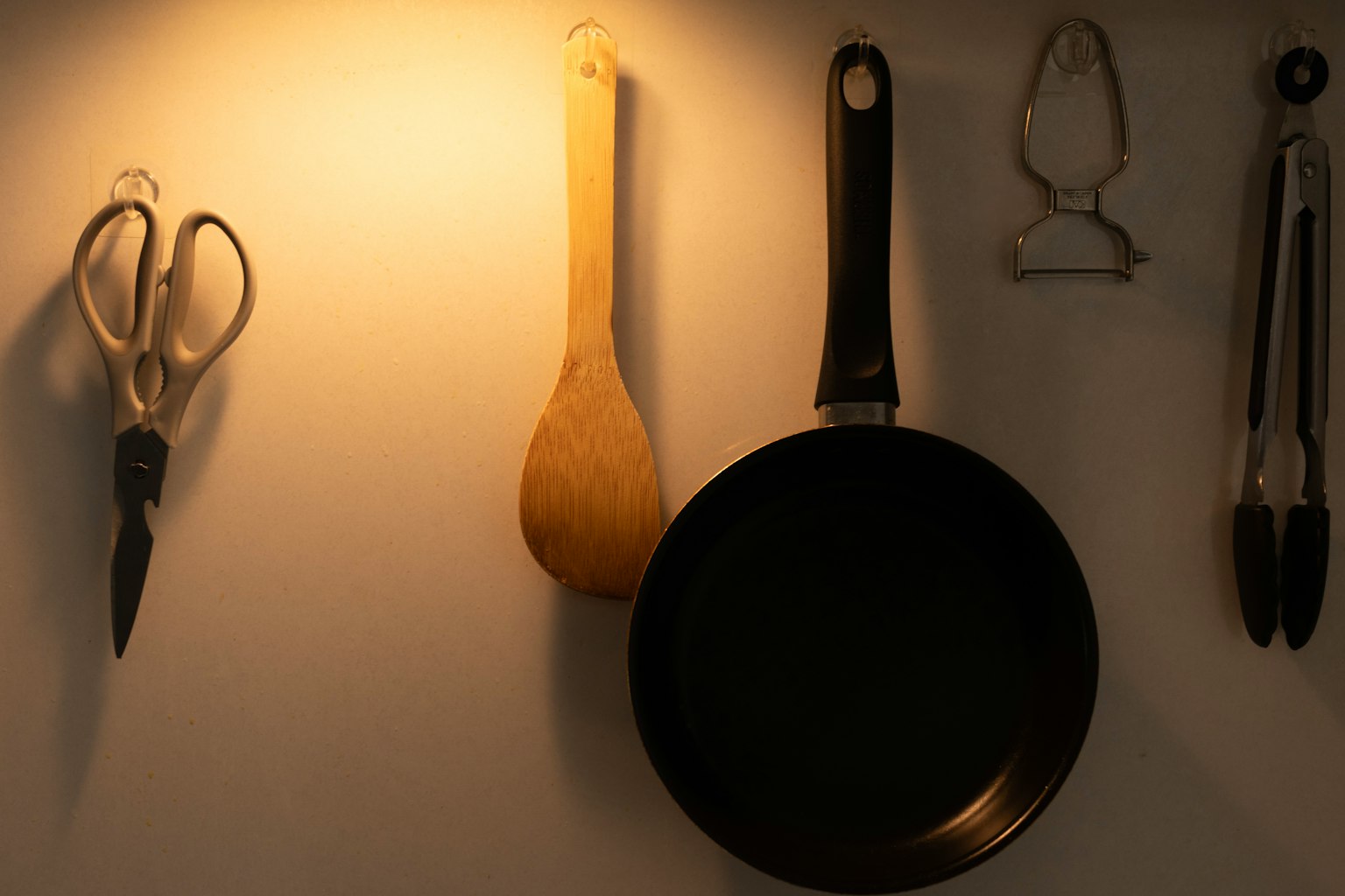 Set di utensili da cucina appesi a un muro tra cui forbici cucchiaio di legno padella pelapatate pinze