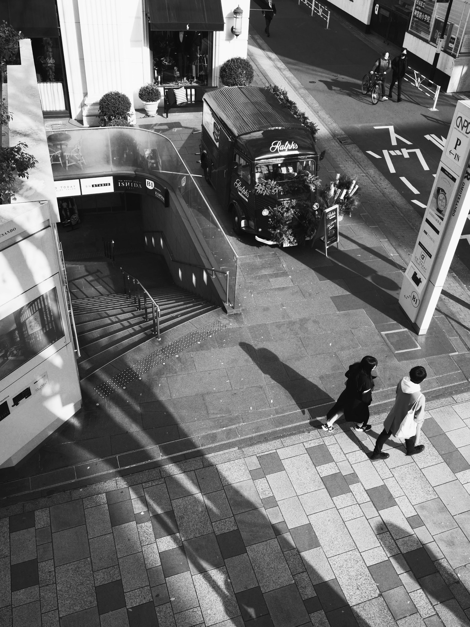 Städtische Szene in Schwarzweiß mit gehenden Menschen sichtbarer U-Bahneingang und Bus