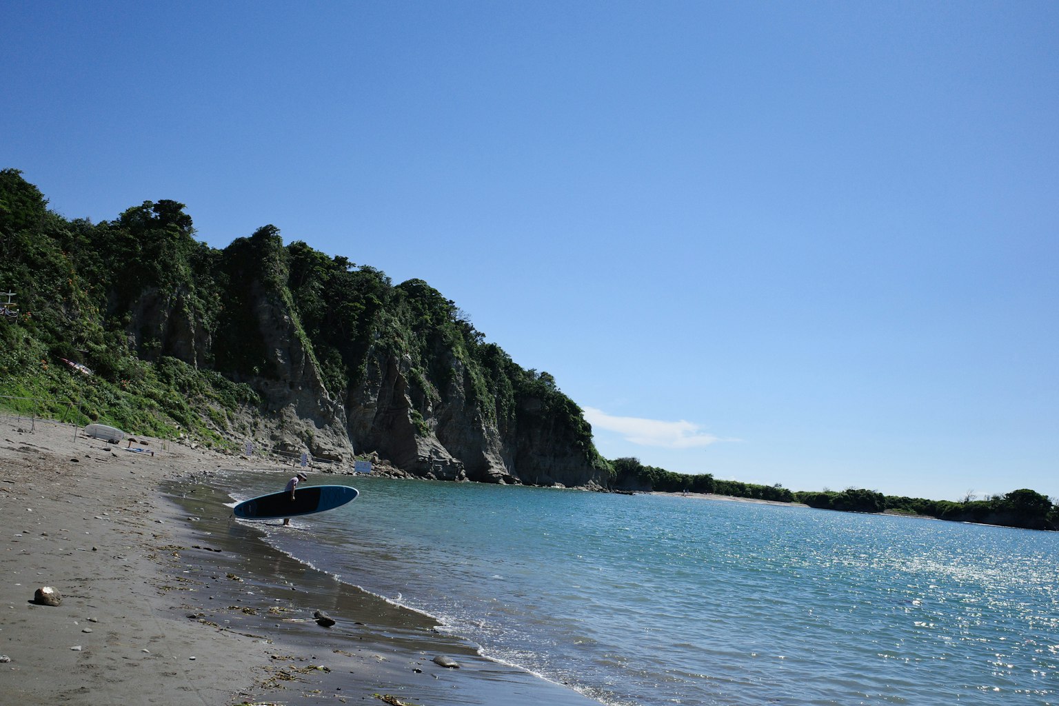 Beach scene with blue sky and calm sea featuring a boat and green cliffs