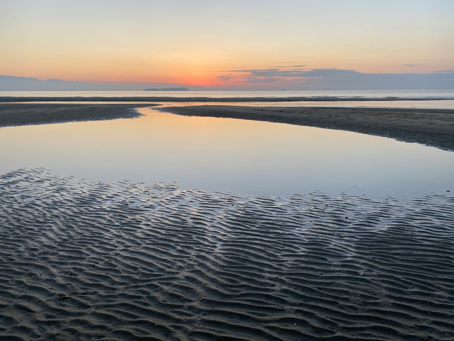 Scena di spiaggia serena con riflessi del tramonto e motivi di sabbia