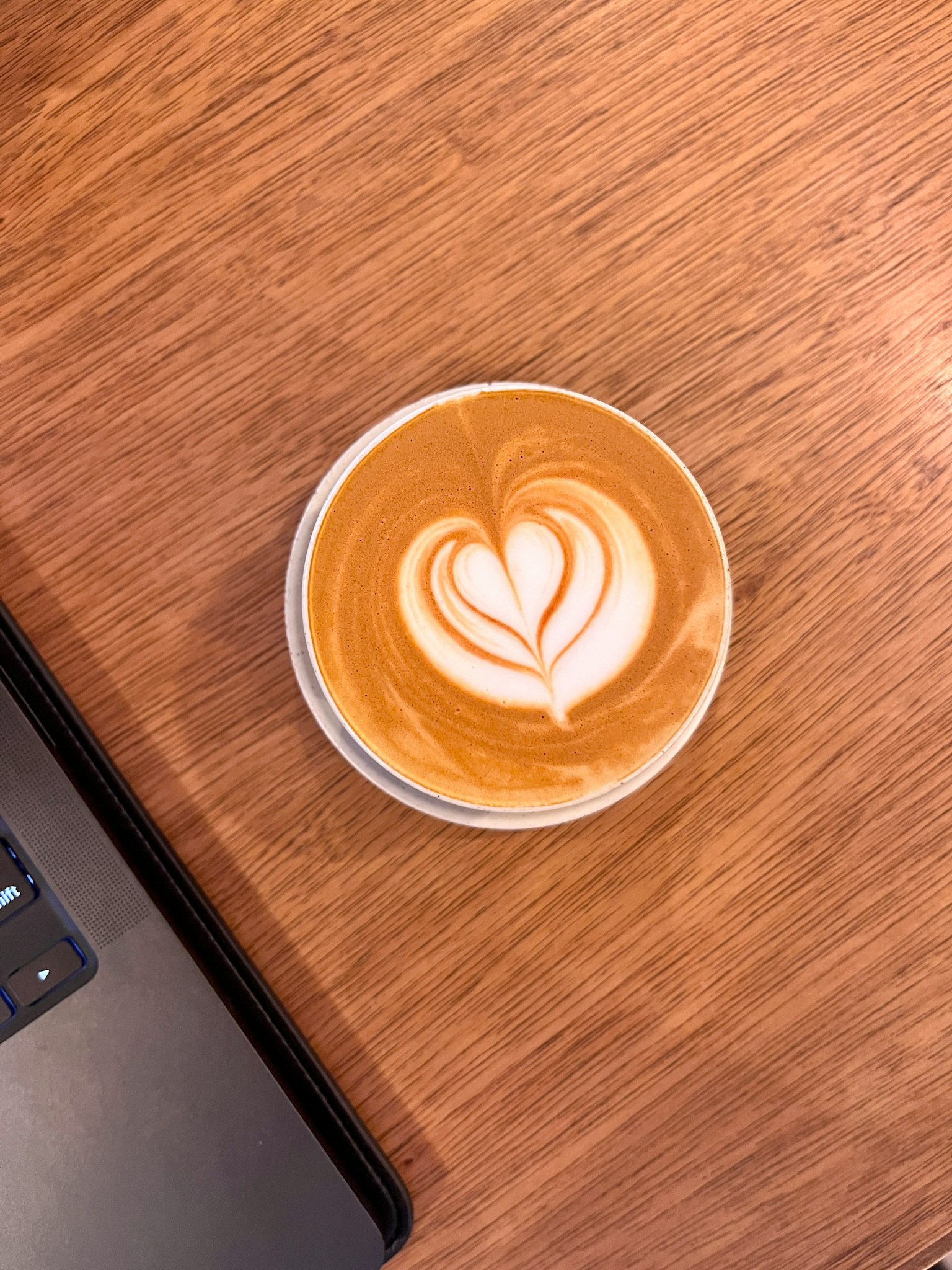 Secangkir latte art dengan desain hati di atas meja kayu