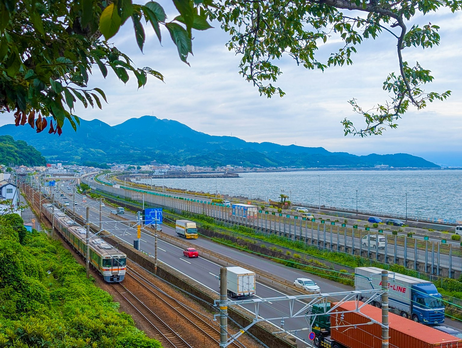 沿海岸线的铁路和公路风景 背景中有绿色树木和山脉