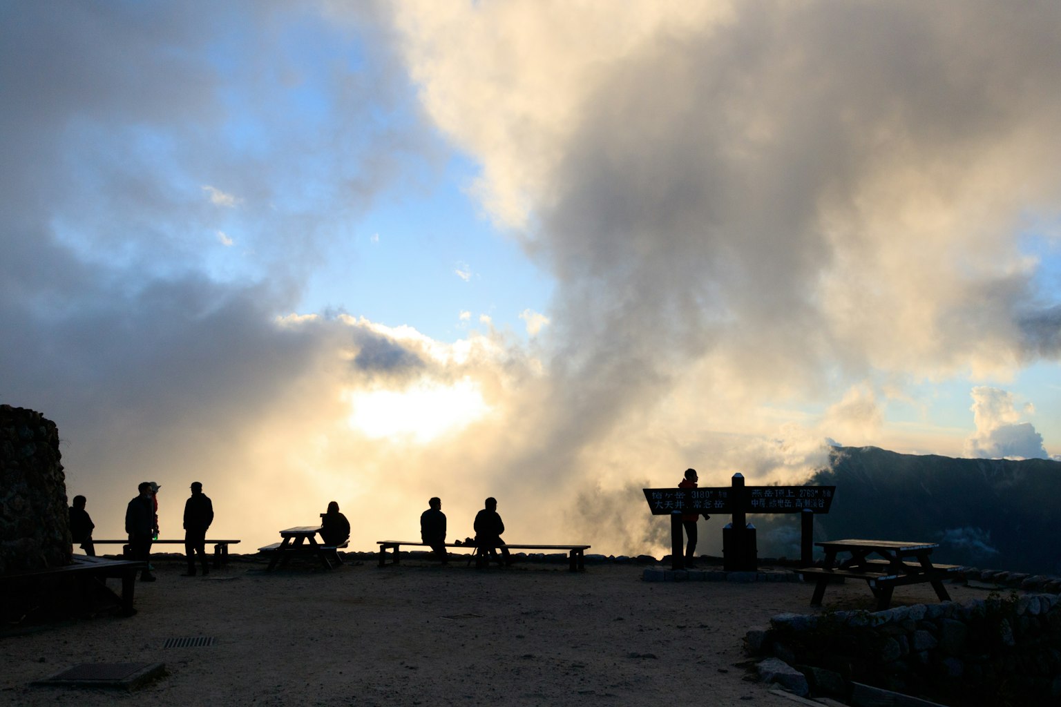 Silhouette orang dan bangku di titik pandang gunung dengan awan dramatis