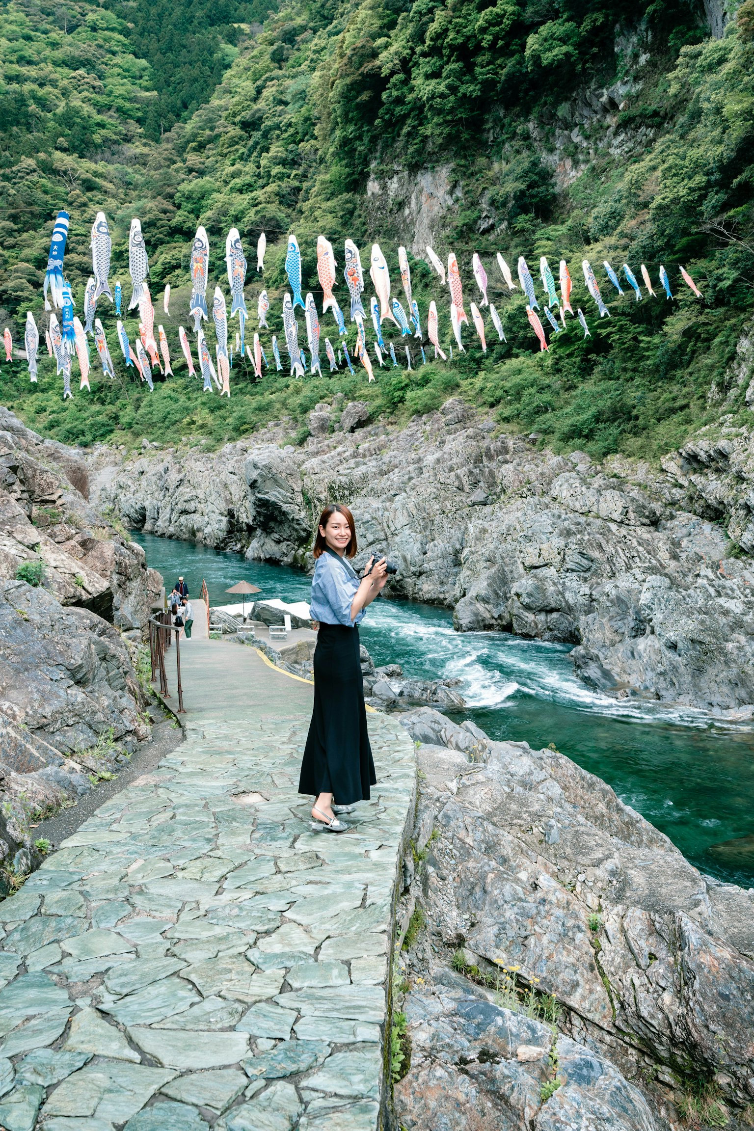 一个女人站在河边，头上悬挂着五彩斑斓的鲤鱼旗