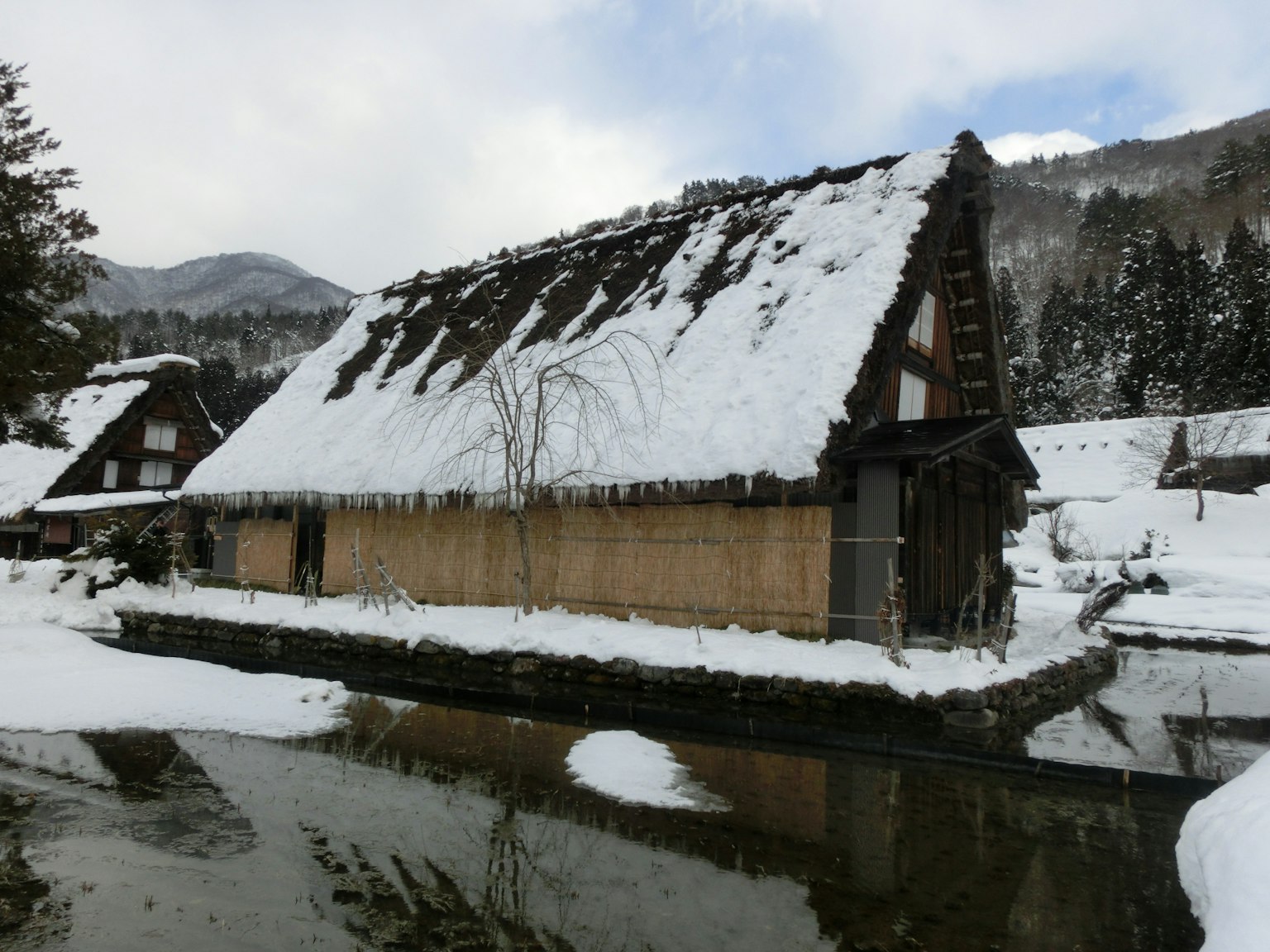 Maison gassho-zukuri couverte de neige au bord d'une surface d'eau calme