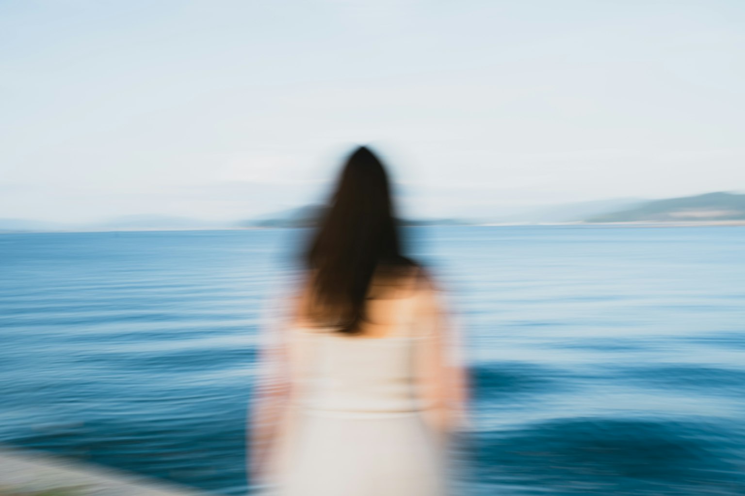 Silhouette of a woman gazing at the sea with a blurred background of blue water and sky