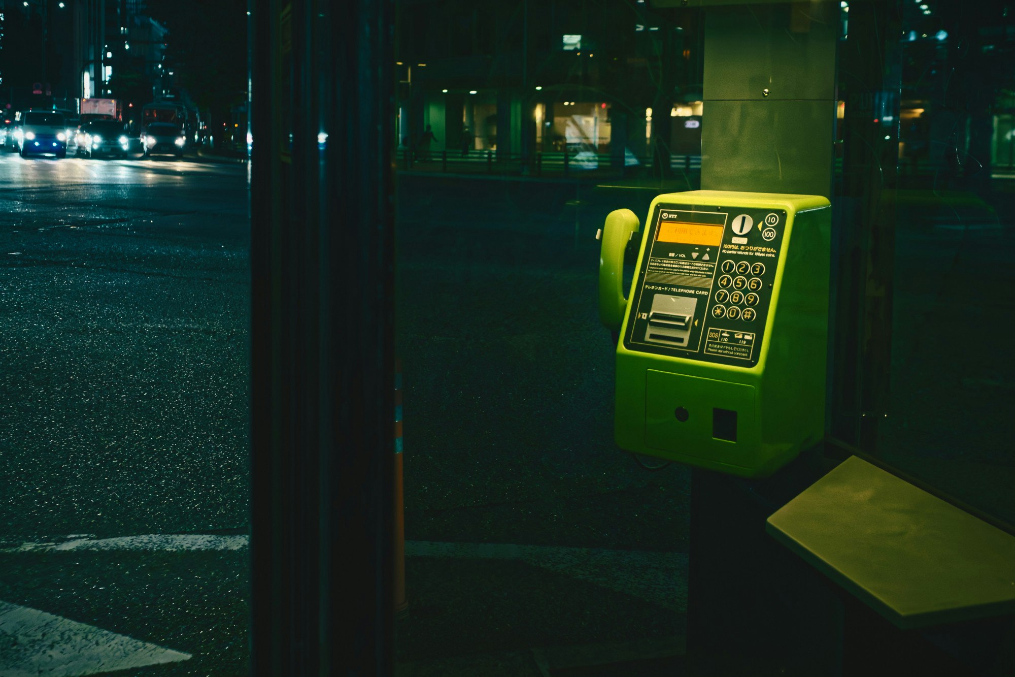 夜の街角に置かれた緑の公衆電話ボックスのある風景
