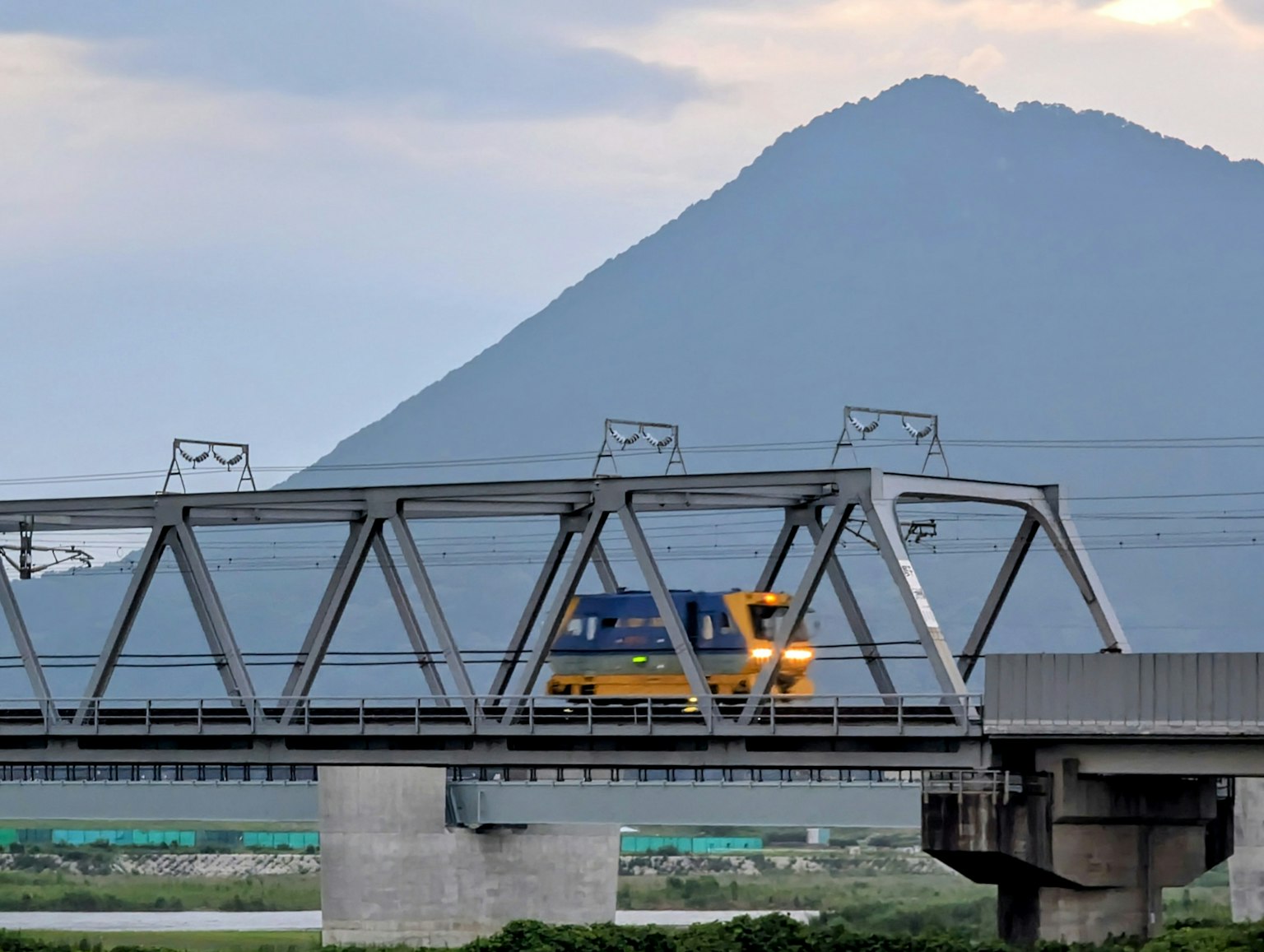 Tren amarillo cruzando un puente ferroviario con una montaña de fondo