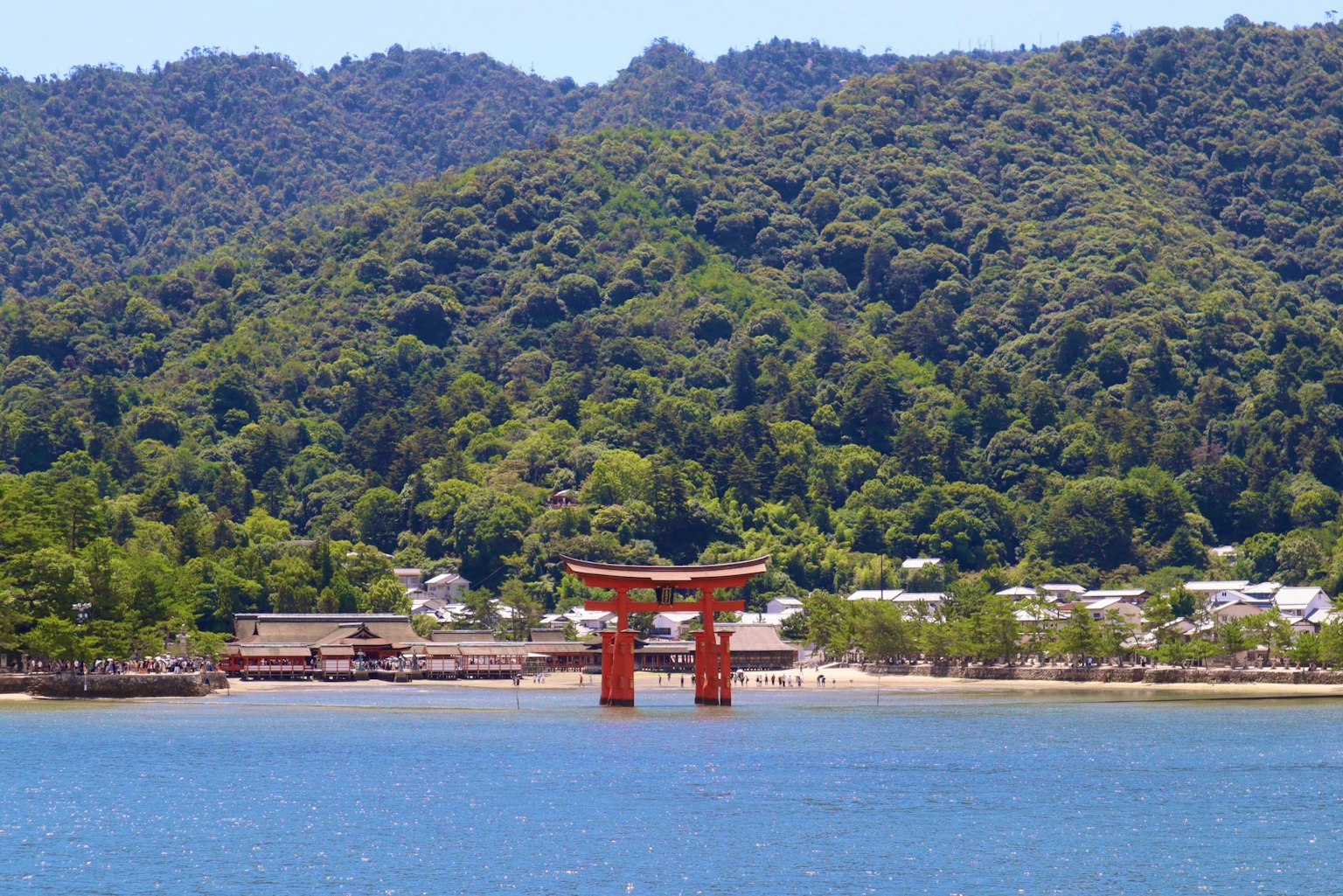 红色鸟居矗立在蓝色水面上，背景是绿色山脉
