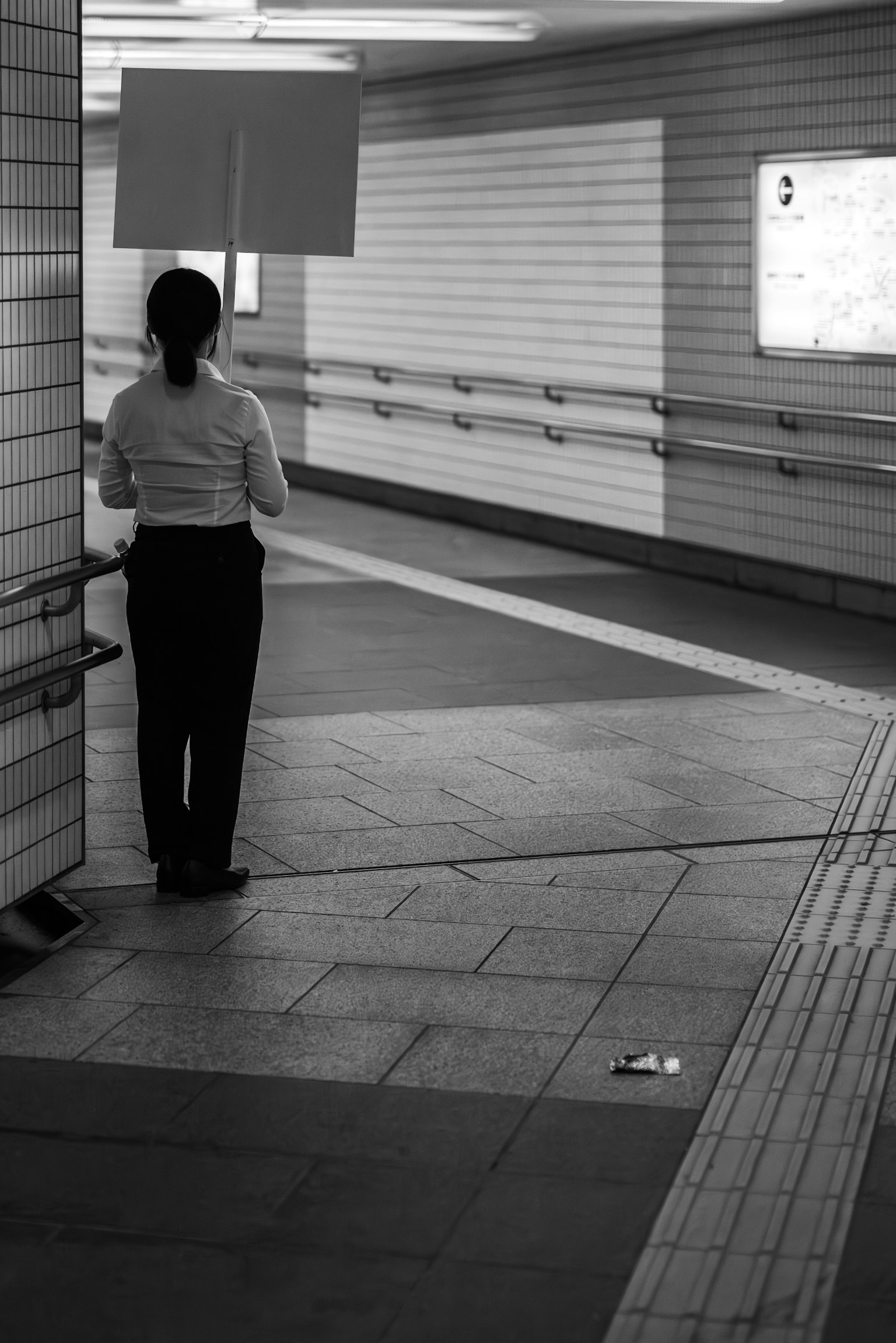 Una persona con un cartello si trova in un passaggio sotterraneo in bianco e nero