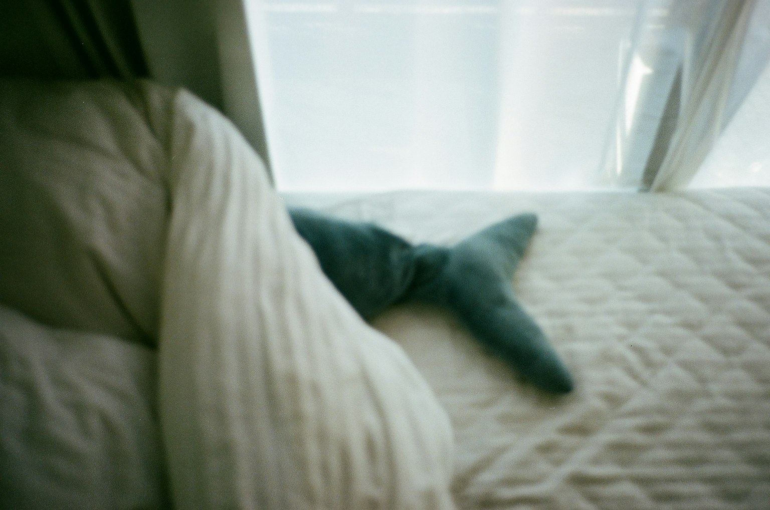 Immagine di un cuscino blu a forma di coda di pesce su un letto con biancheria bianca