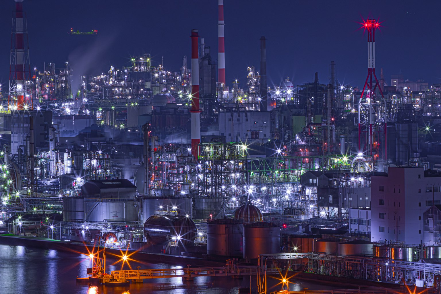 Area industriale notturna con ciminiere e serbatoi luminosi