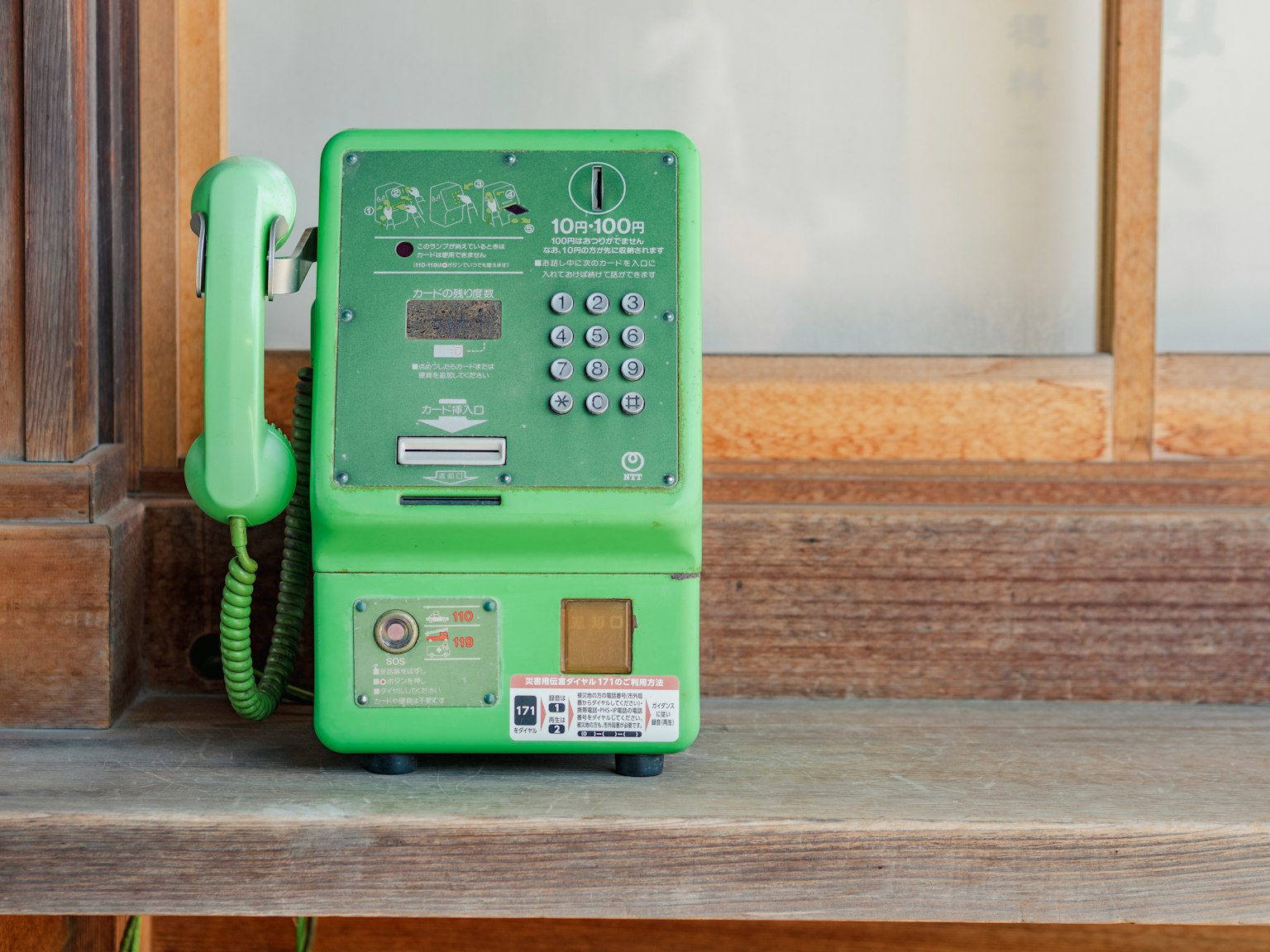 Telepon umum hijau diletakkan di atas rak kayu