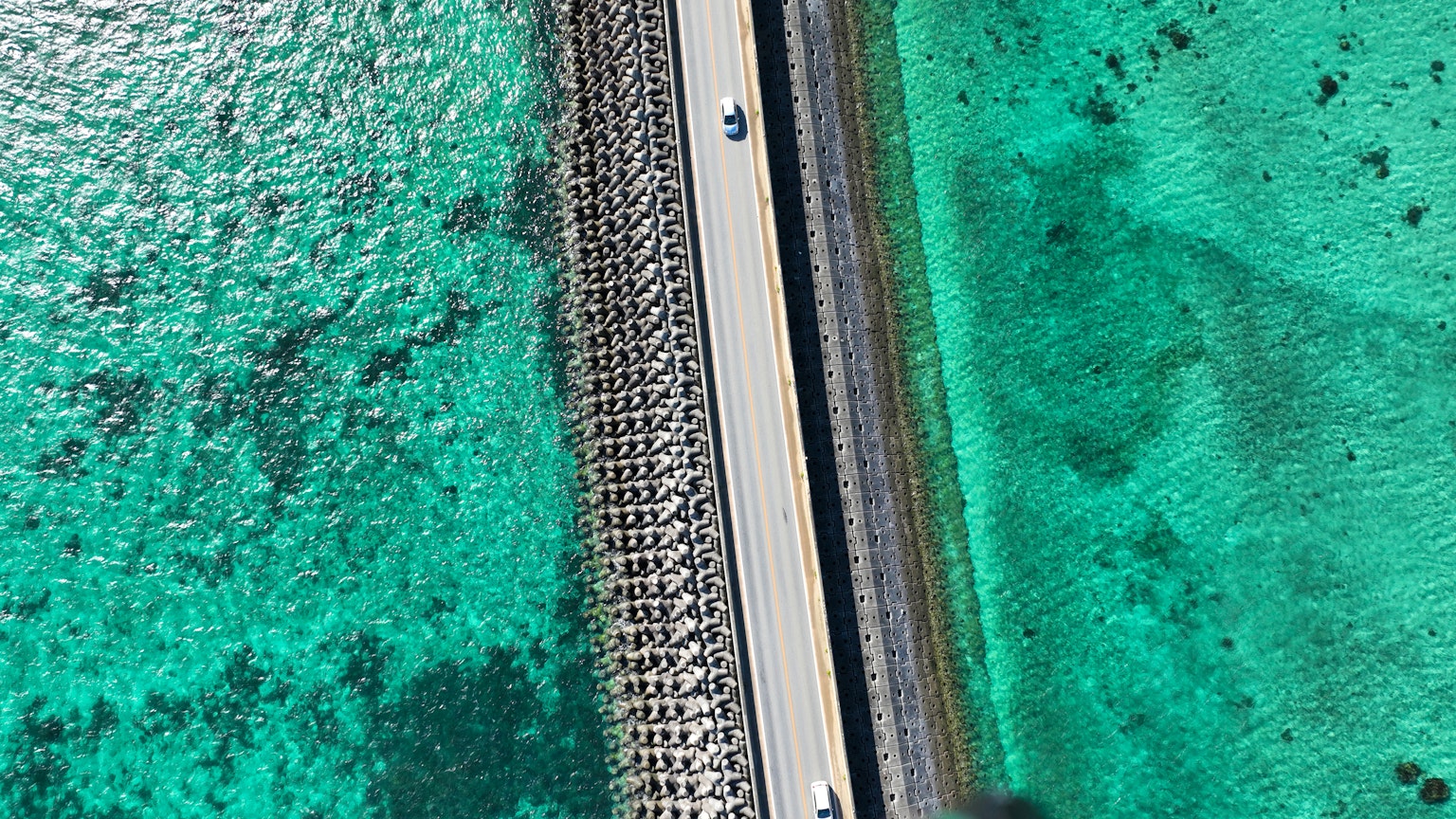 Vista aérea de una carretera blanca y un muelle de piedra sobre agua turquesa