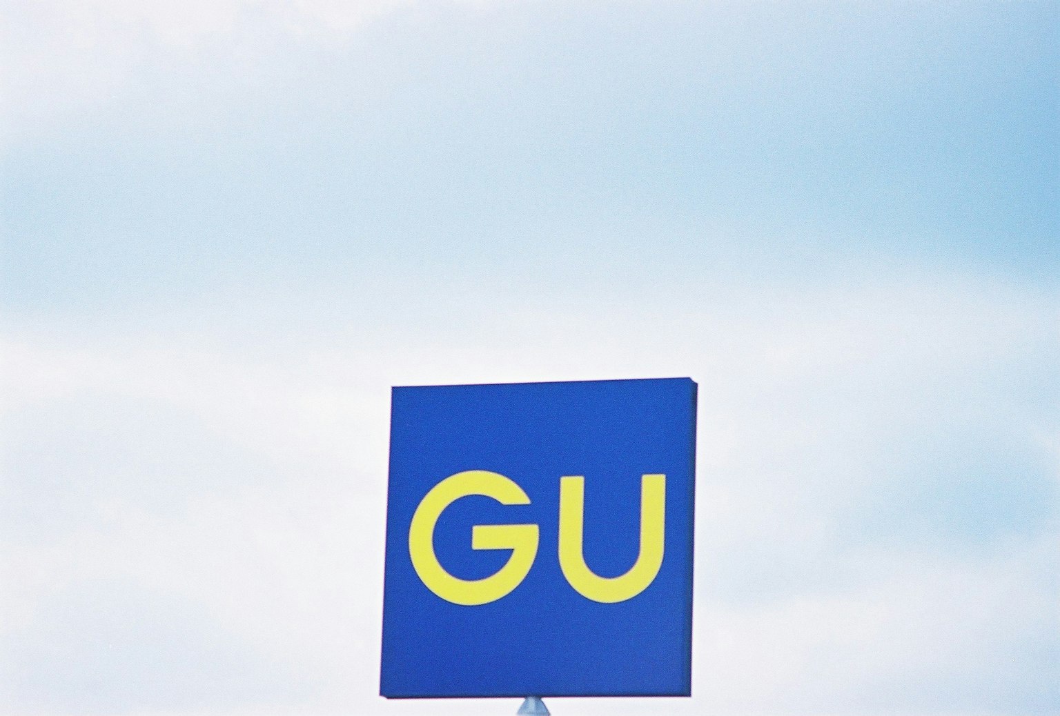 Un panneau bleu avec de grandes lettres jaunes affichant le texte GU