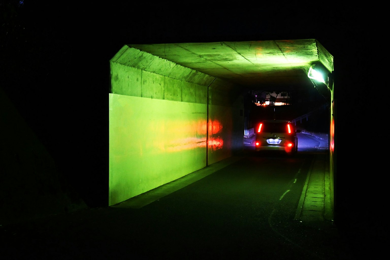 Ein Auto fährt in einen dunklen Tunnel mit bunten Lichtern, die an den Wänden reflektieren