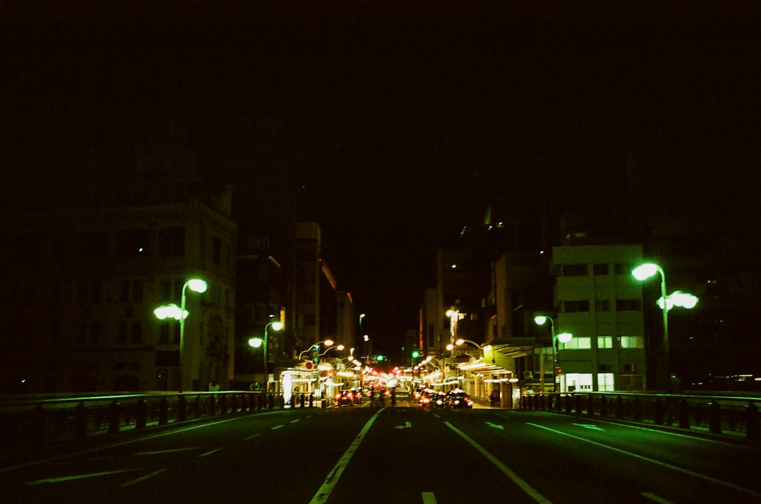 Paesaggio urbano notturno con lampioni verdi lungo la strada e edifici visibili