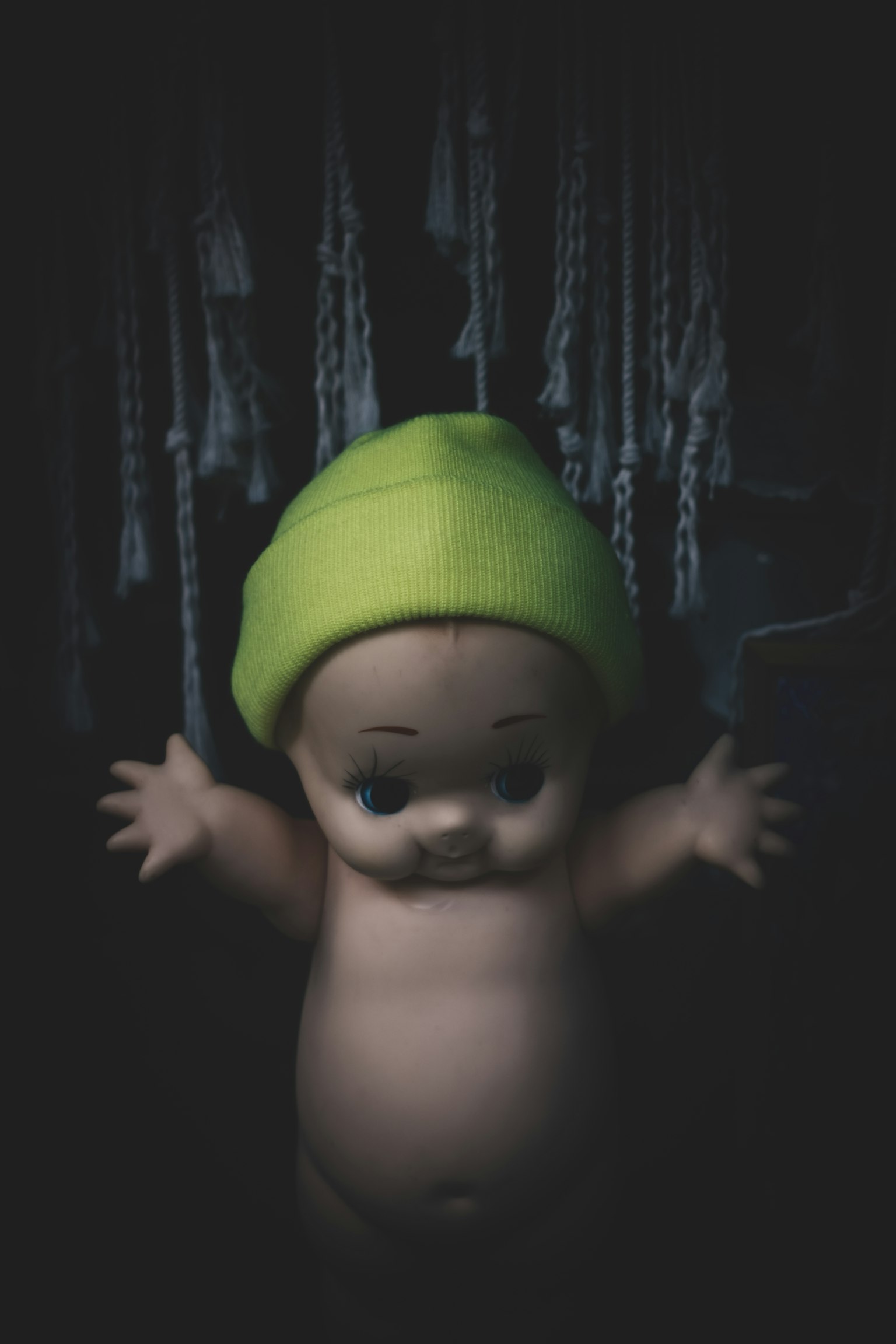 Boneka yang mengenakan topi hijau berdiri di depan latar belakang gelap