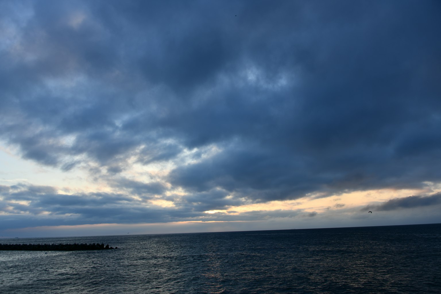 暗い雲が広がる海の風景に夕焼けの光が差し込む