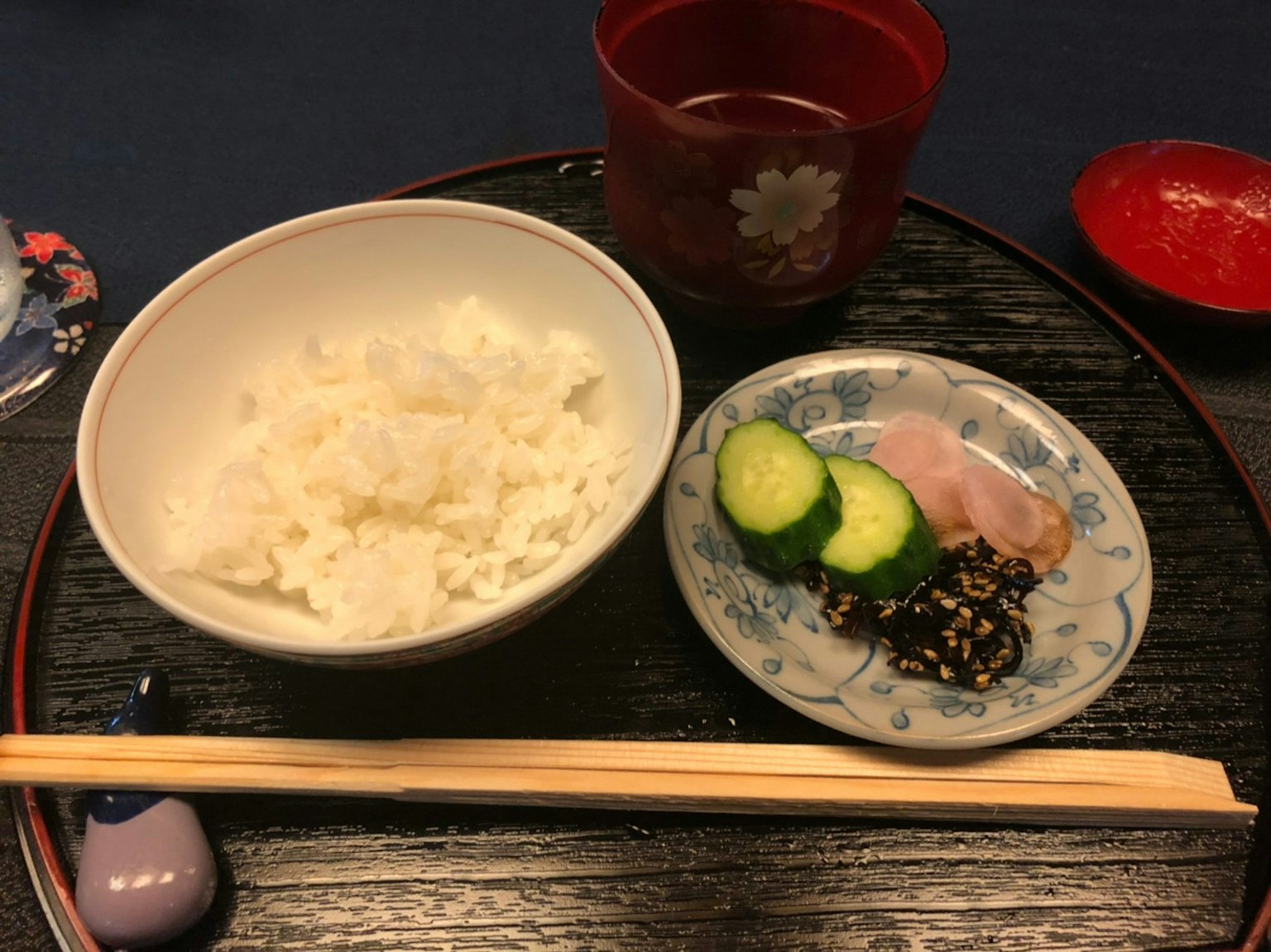 一个装有白米饭、黄瓜和火腿的盘子，旁边有一个红色茶杯