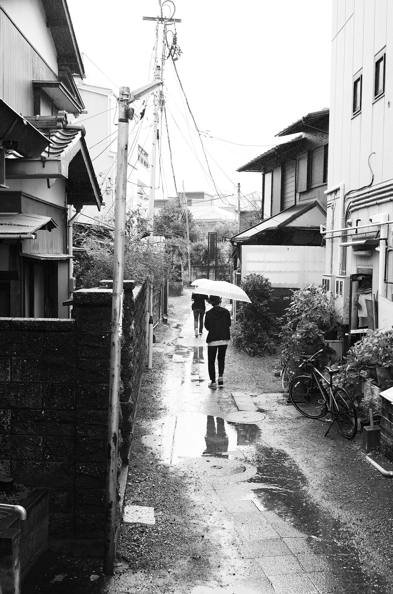 คนเดินในซอยแคบใต้ฝนถือร่มในฉากขาวดำ