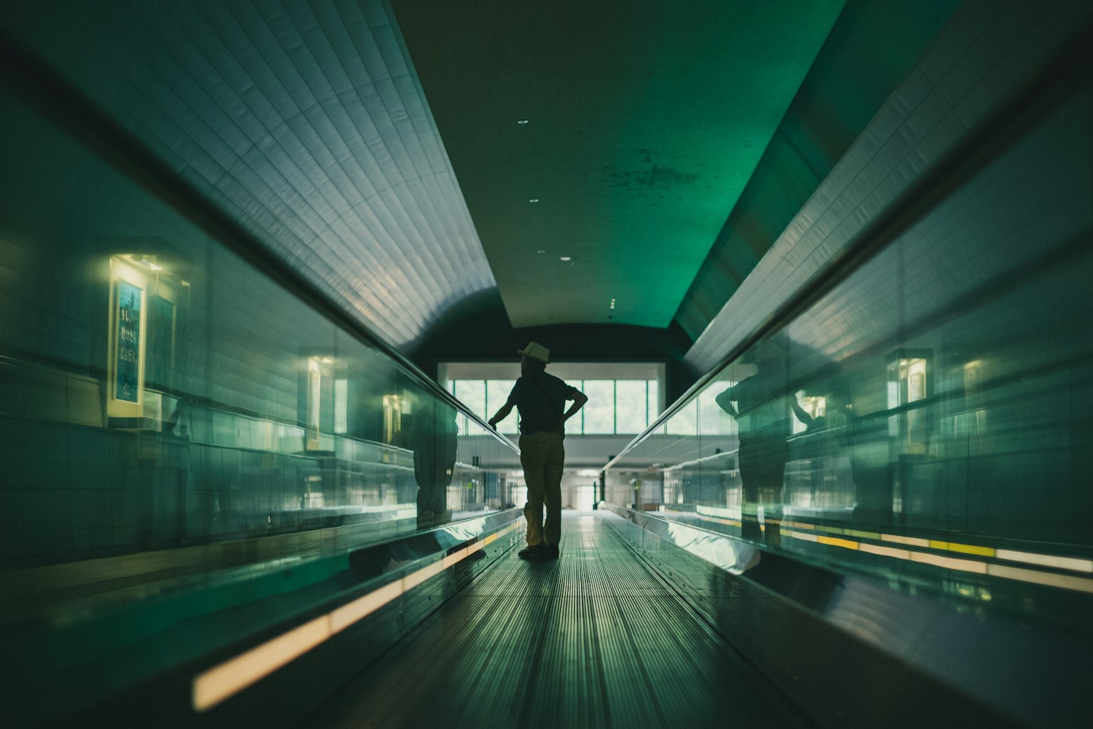 A person standing in a long corridor under green lighting