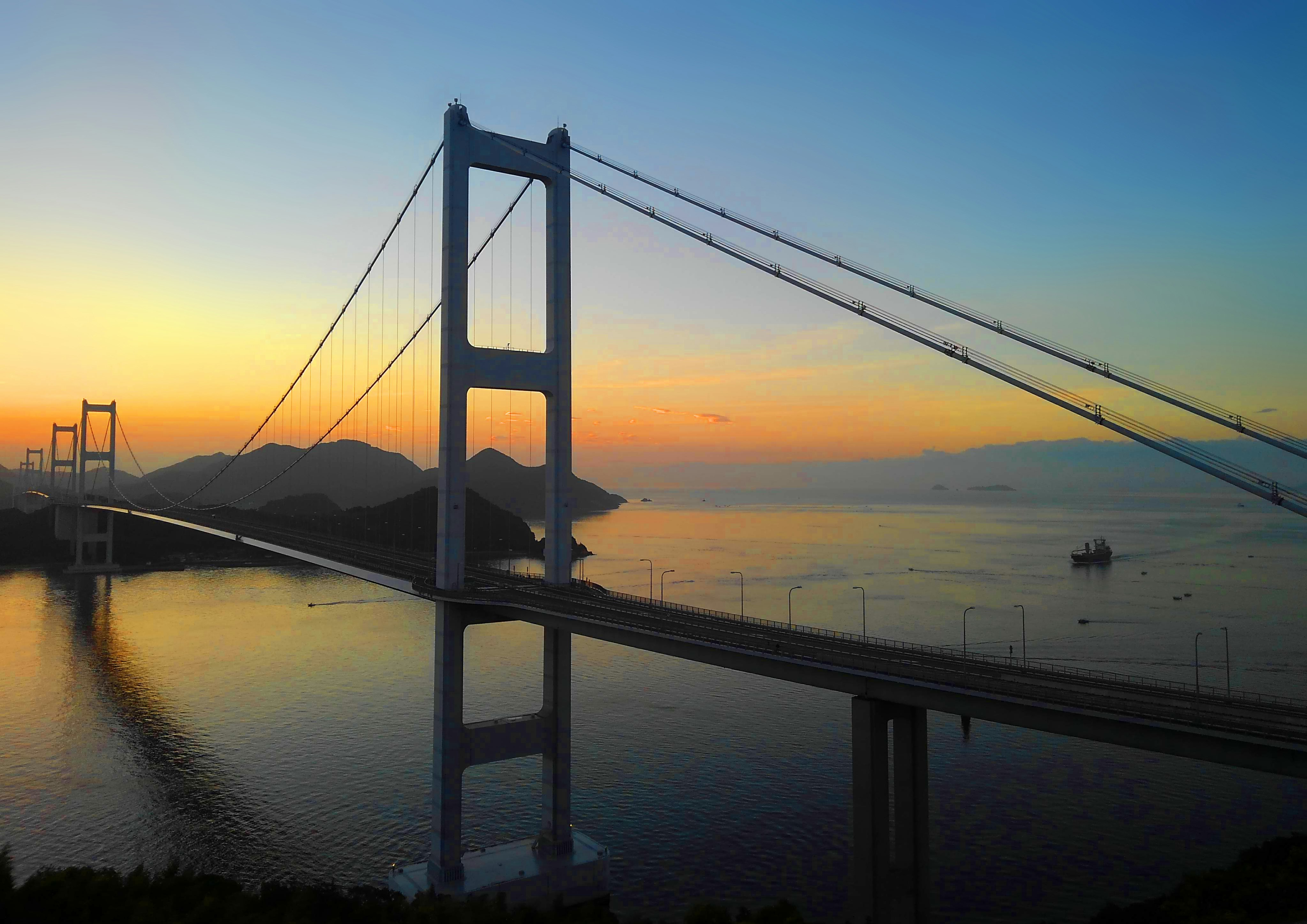濑户内海上“濑户内海海道（しまなみ海道）”的夕阳下悬索桥与平静水面