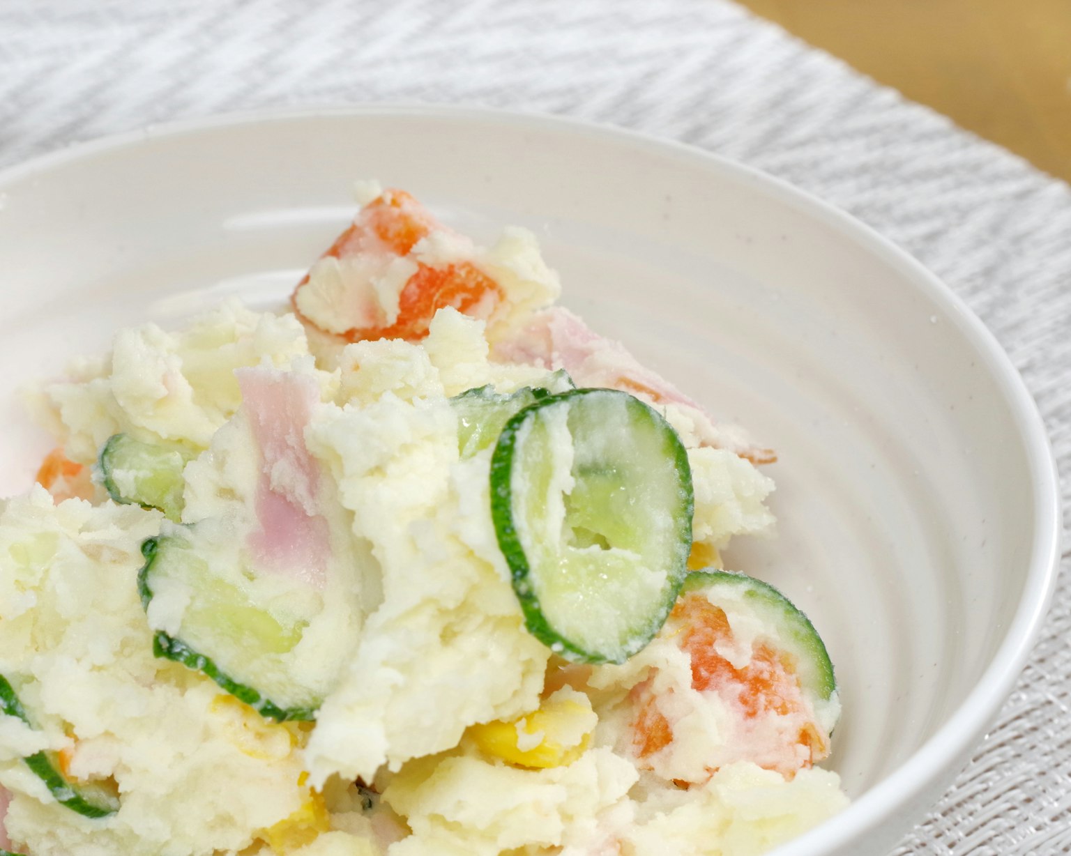 Potato salad in a white bowl with cucumber and carrot toppings