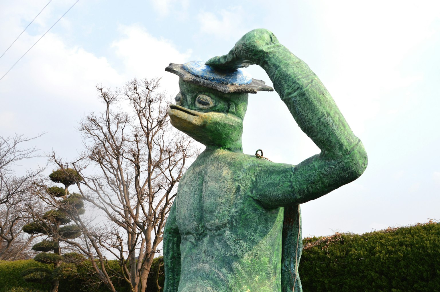 Green frog-like sculpture holding a hat
