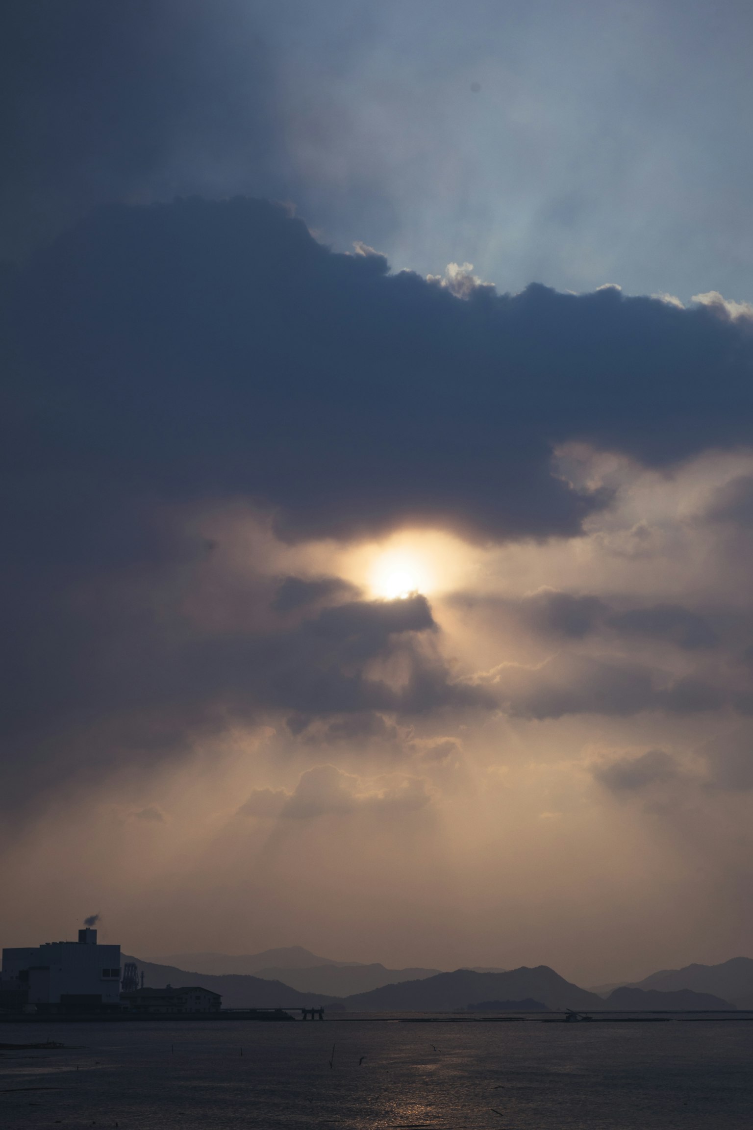 Un paisaje con el sol visible a través de cielos nublados nubes brumosas y montañas oscuras a lo lejos