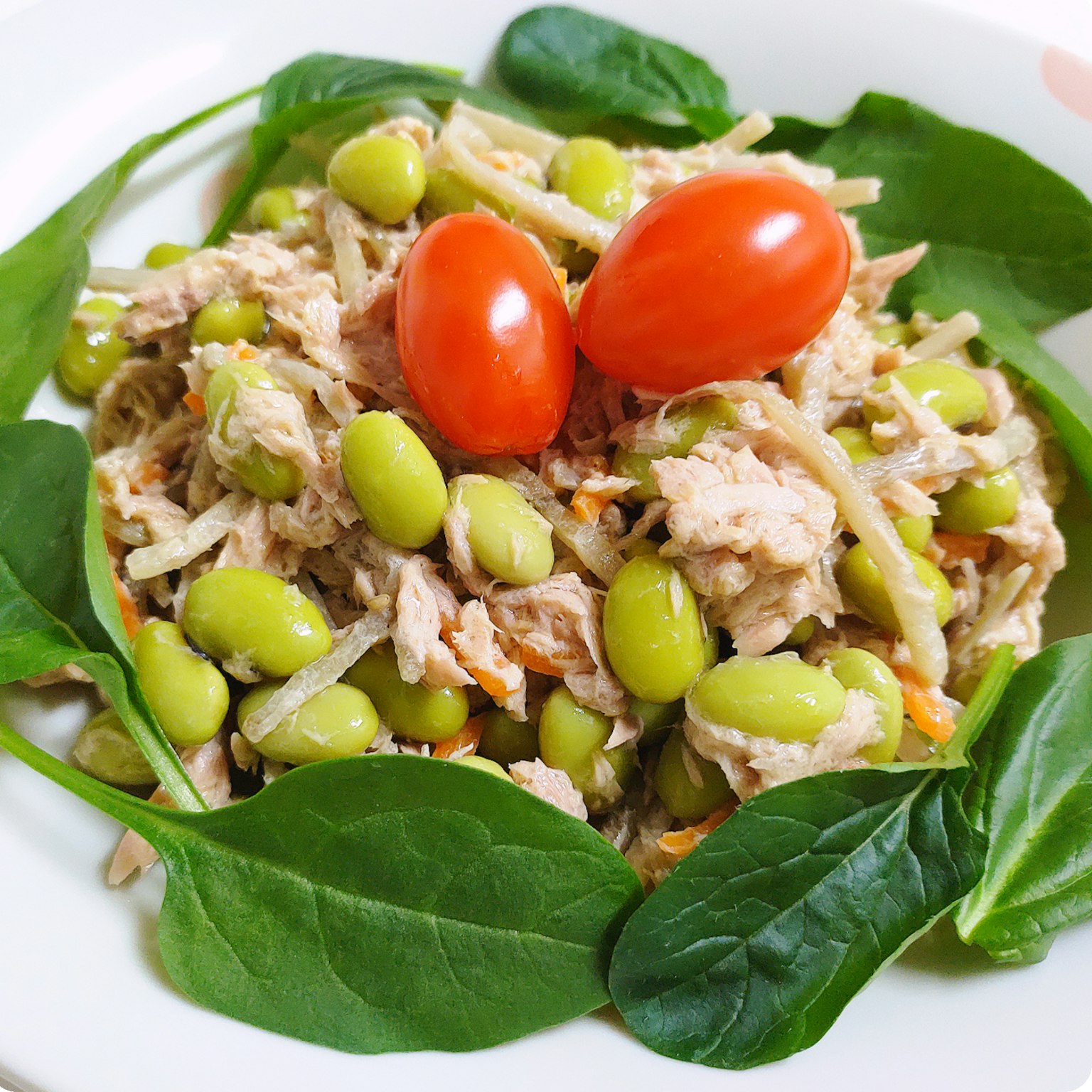 Thunfisch-Edamame-Salat mit Kirschtomaten auf einem Bett aus Spinat