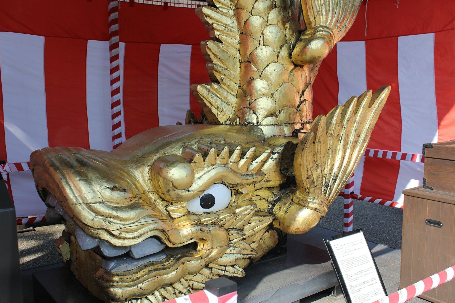 Escultura de dragón dorado exhibida frente a cortinas rojas y blancas