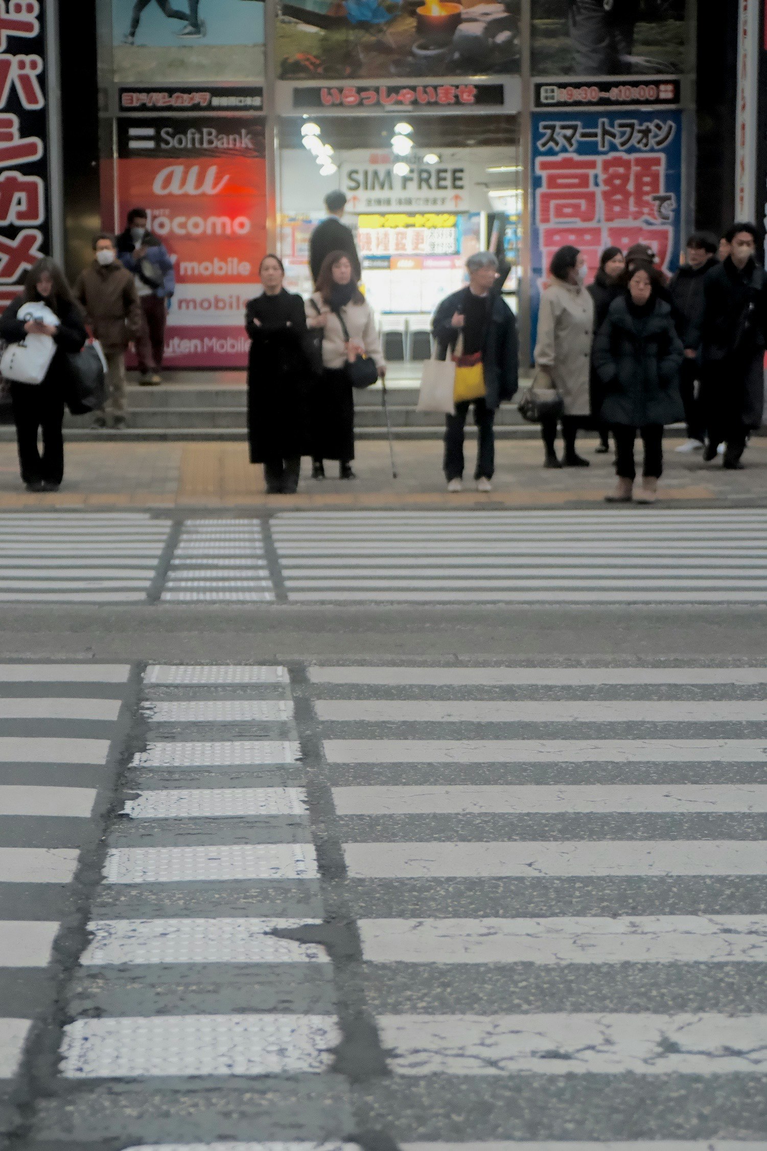 横断歩道を歩く人々と携帯ショップの看板が並ぶ街角